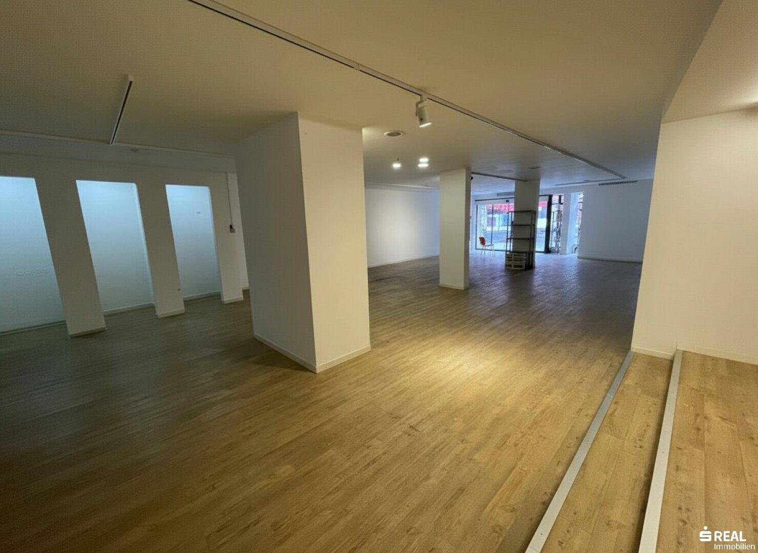 Weitläufiger Gewerberaum mit Holzboden und großen Fensterfronten, bietet vielseitige Gestaltungsmöglichkeiten für Kunden.