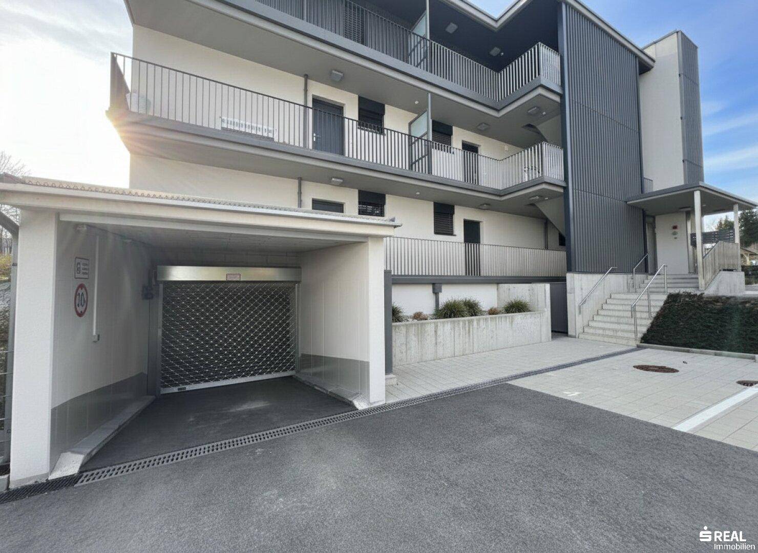 Außenansicht des Gebäudes mit Tiefgaragenzufahrt und modernem Eingangsbereich.