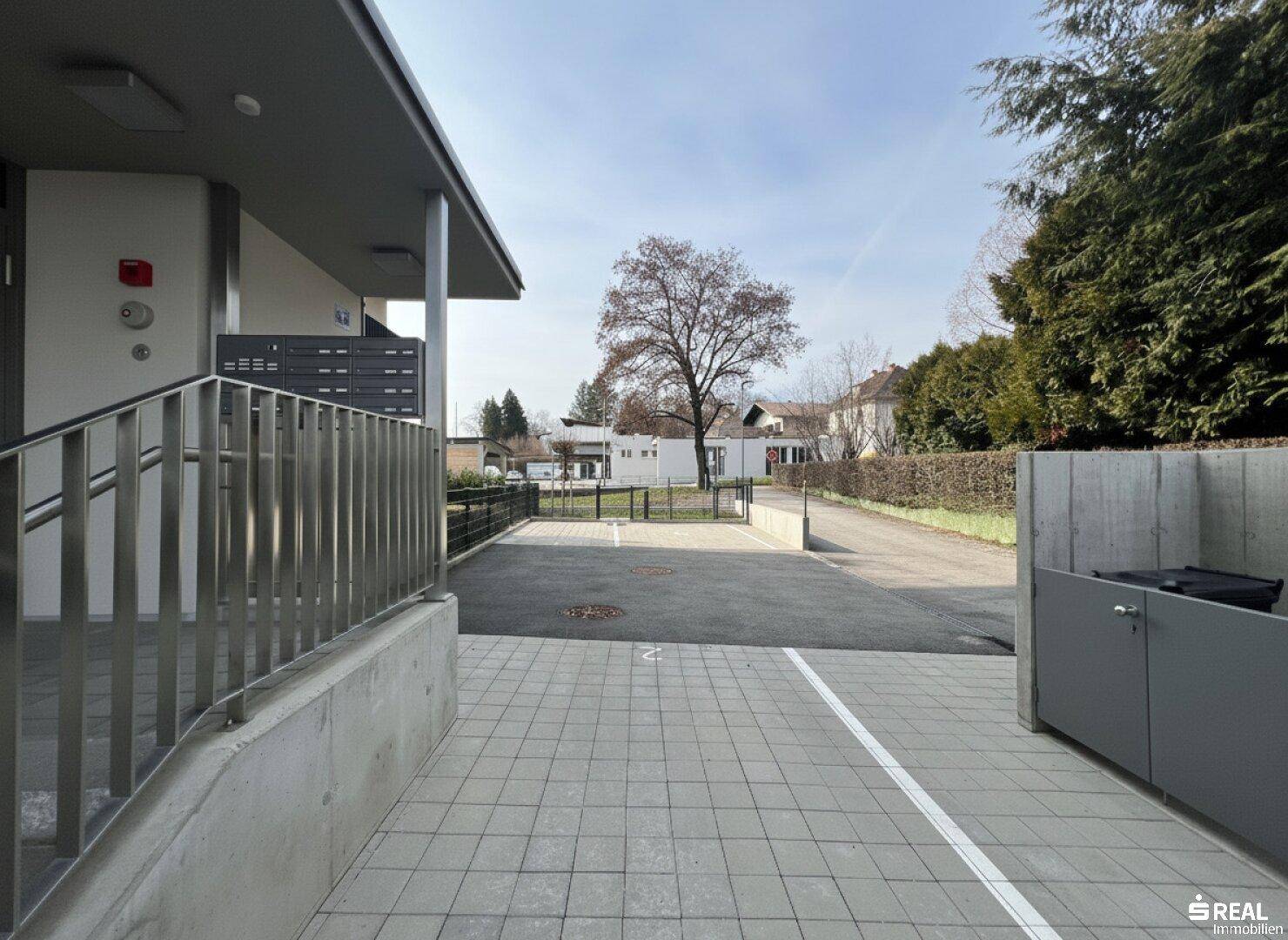 Außenparkplätze vor dem modernen Wohngebäude mit Briefkästen und Zugangsbereich.