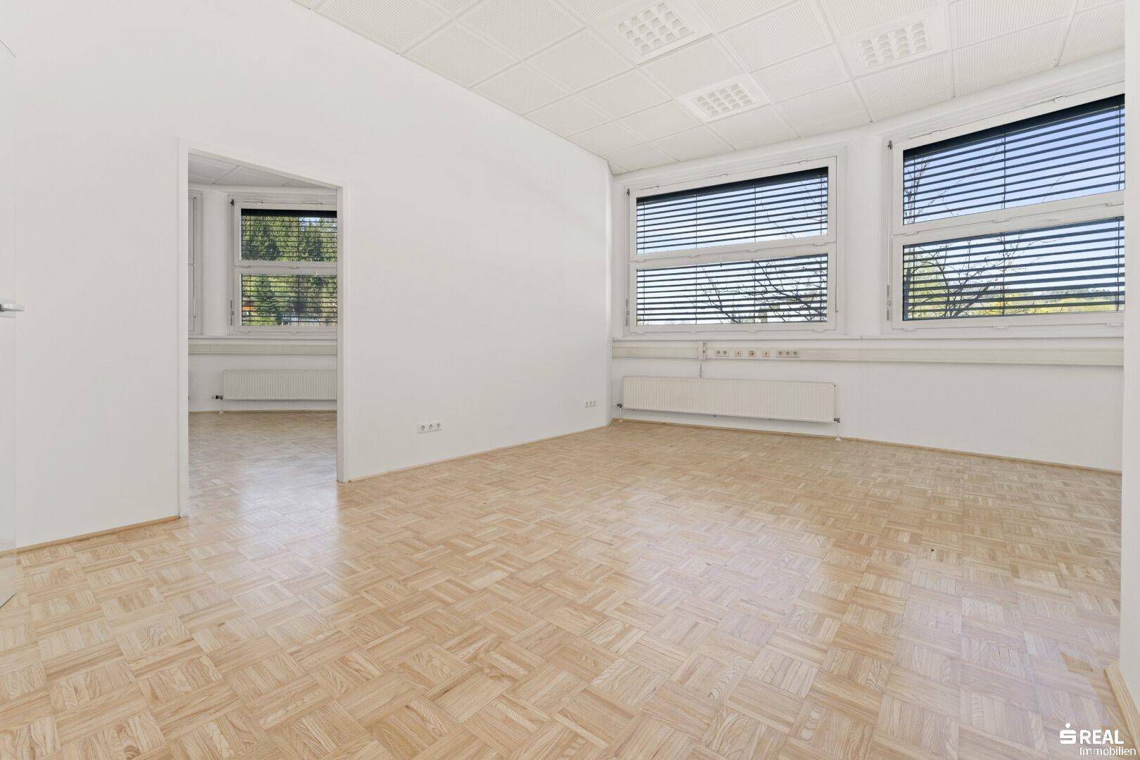 Geräumiger, heller Büroraum mit Parkettboden und mehreren Fenstern, die viel Tageslicht hereinlassen.