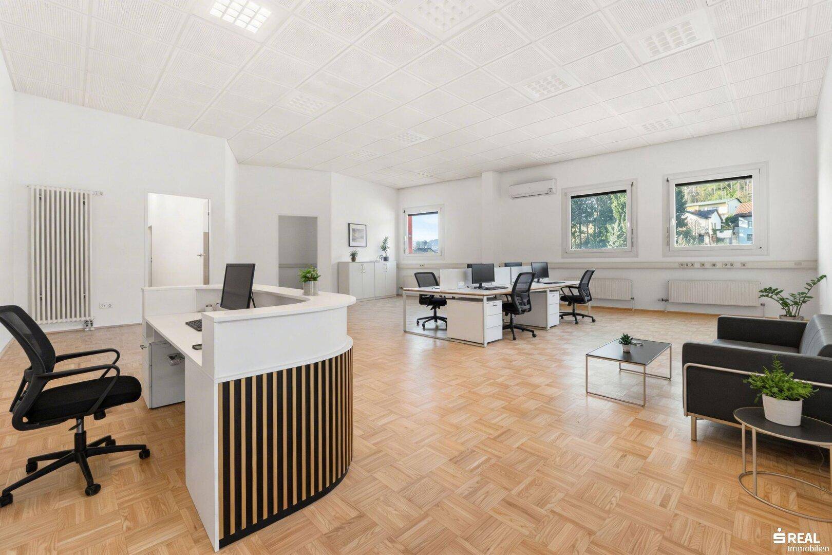 Offener Bürobereich mit Empfangstheke, mehreren Arbeitsplätzen und einer Sitzecke.