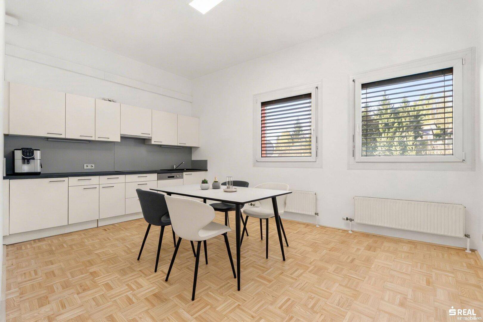Moderne Einbauküche mit weißen Schränken, dunkler Arbeitsplatte und einem Esstisch für Pausen.