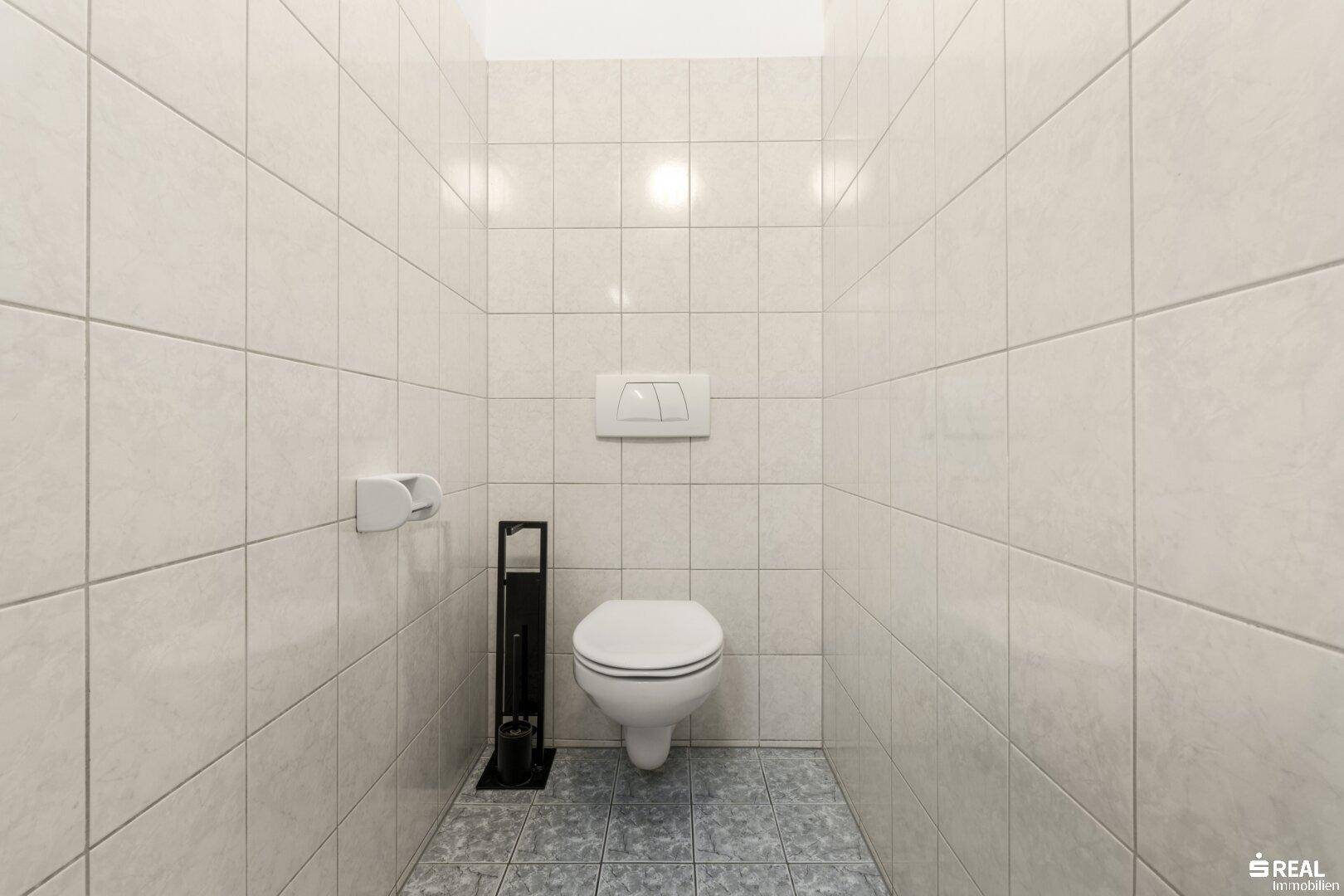 Sauberer Toilettenraum mit hellen Fliesen an Wänden und Boden sowie einer wandhängenden Toilette.