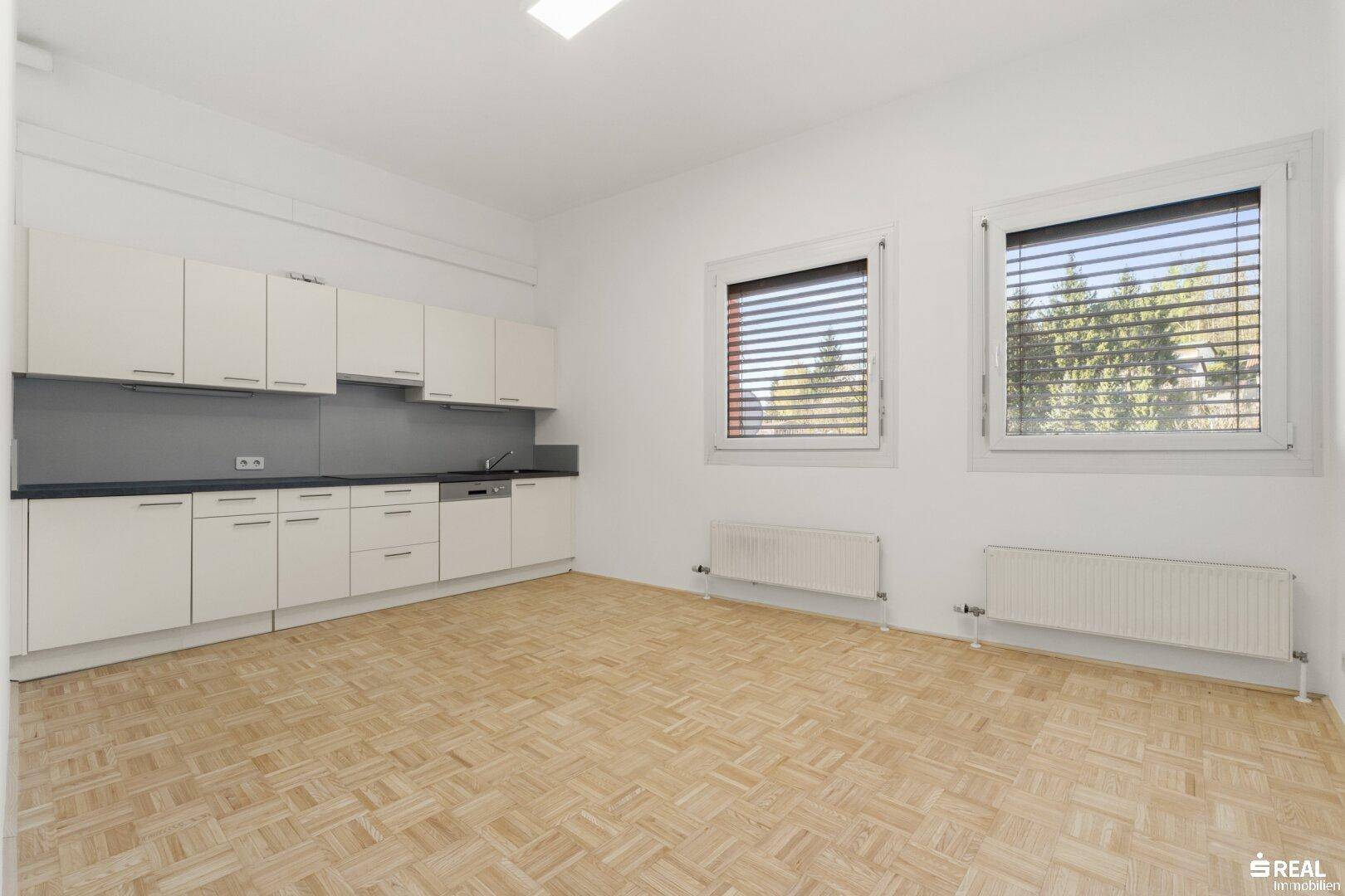 Heller Raum, vorbereitet für eine Küche, mit weißen Schränken, Spüle und Fenstern mit Jalousien.