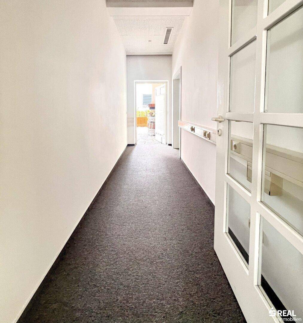 Langer, heller Flur mit Teppichboden und Türen, der zu weiteren Räumen führt.