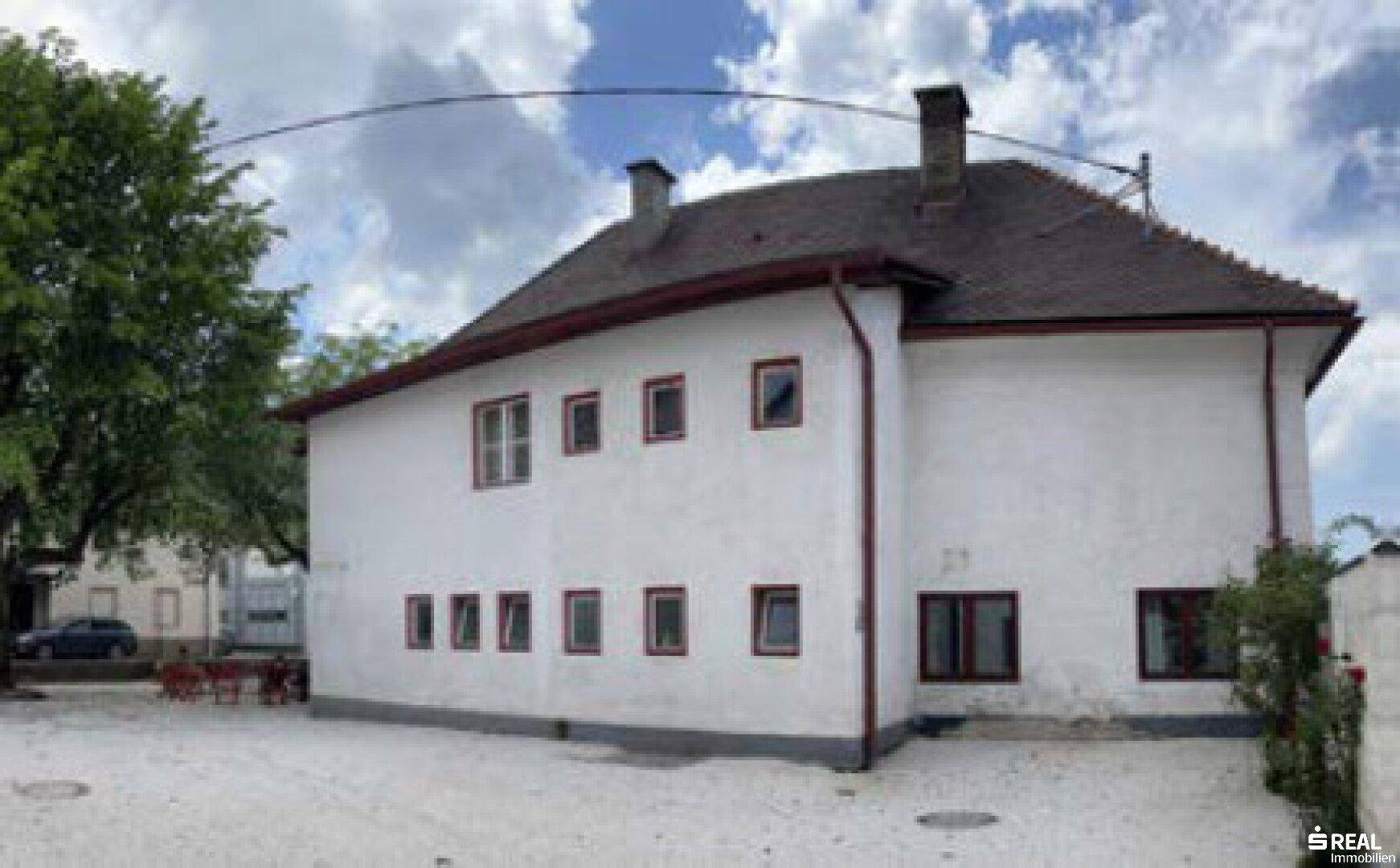 Seitenansicht des historischen Gebäudes mit Schornsteinen und großem Baum im Vordergrund.