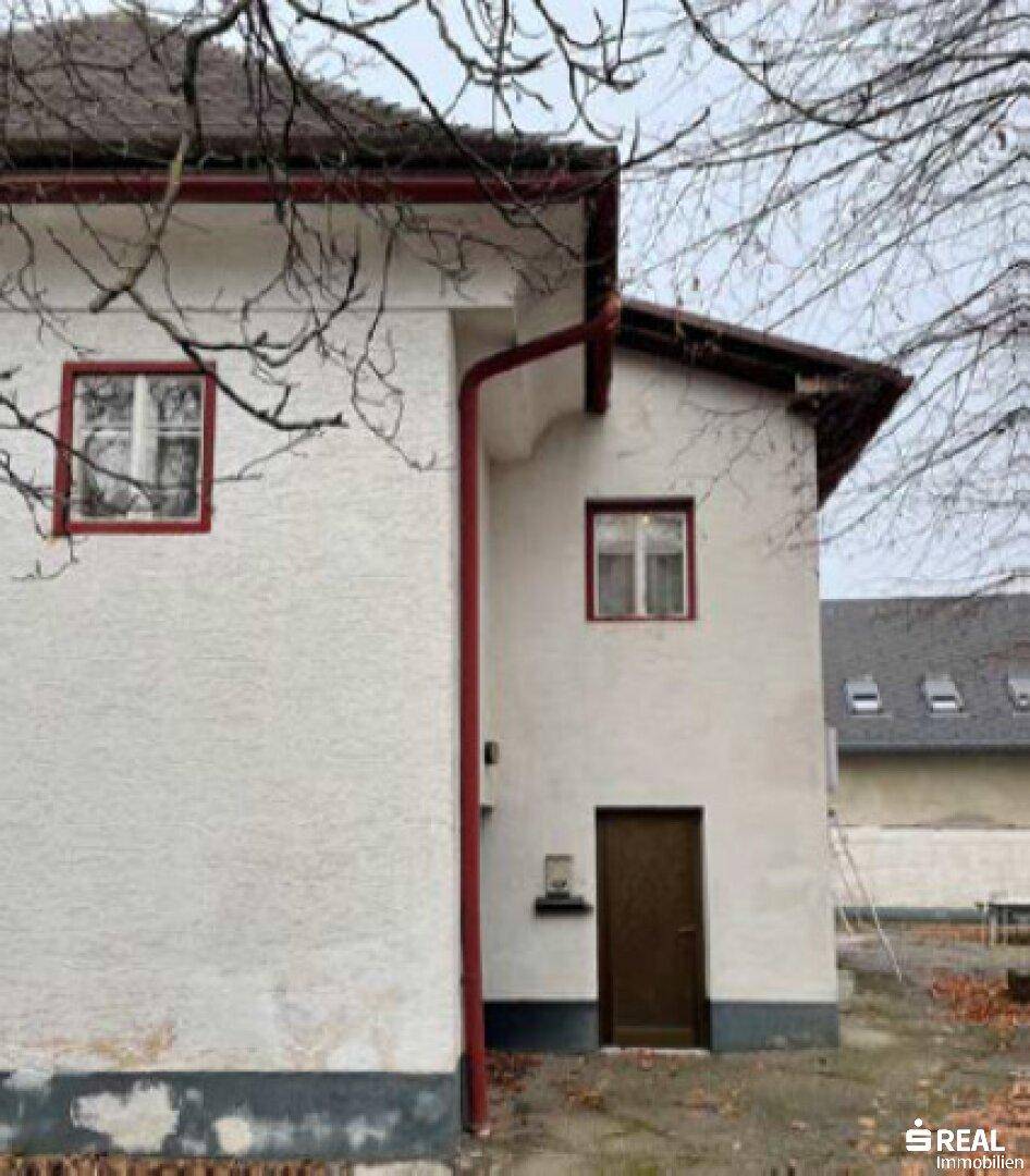 Seitenansicht des historischen Gebäudes im Winter mit kahlen Bäumen und einfacher Eingangstür.