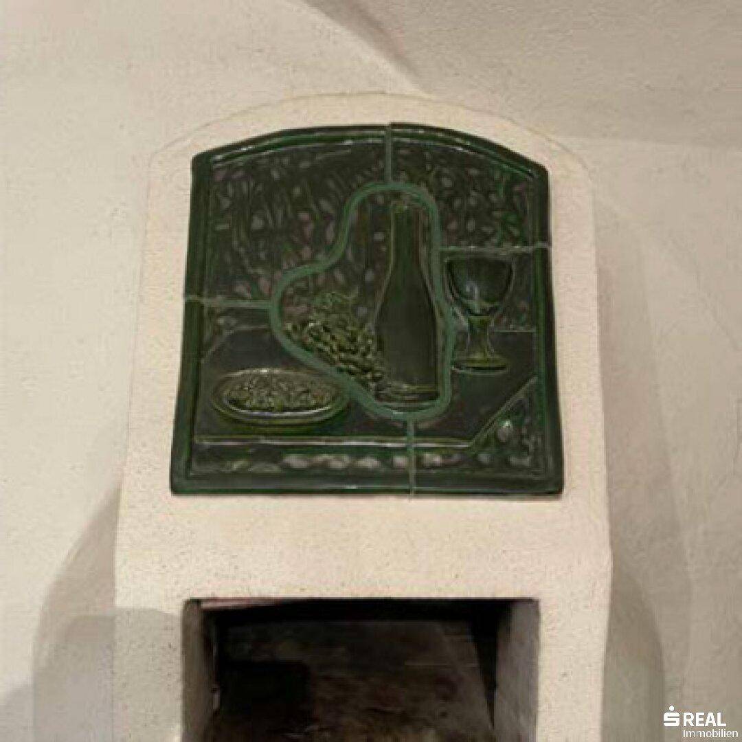 Detailansicht eines traditionellen Kachelofens mit grünen Fliesen und Weinmotiv.