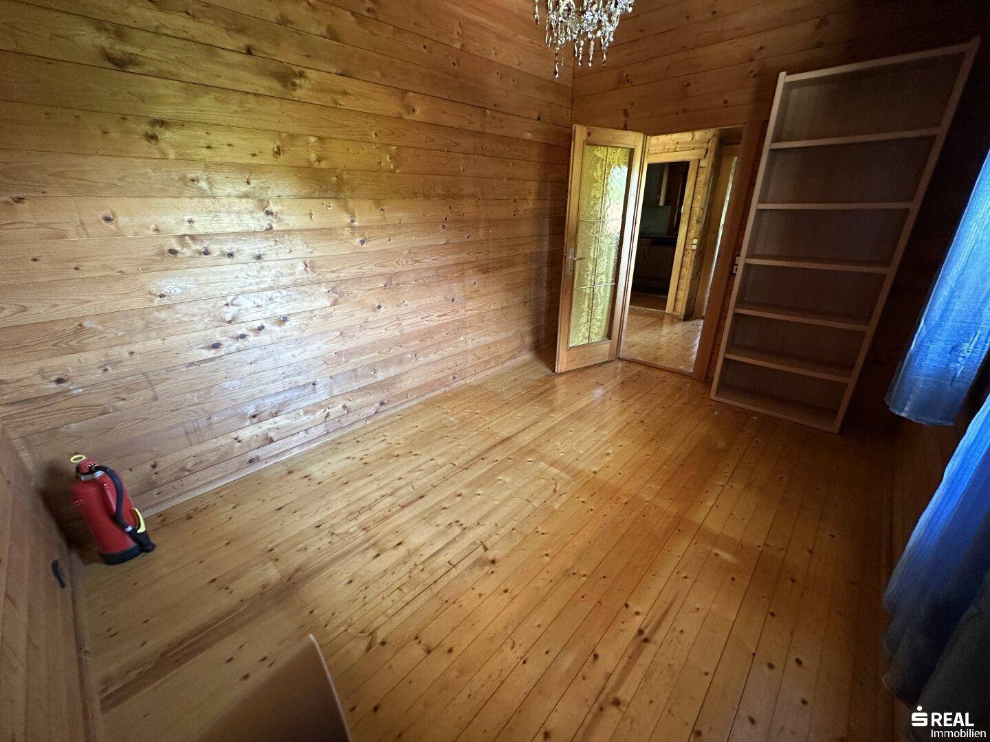 Rustikaler Raum mit Holzwänden und Holzboden, ausgestattet mit einem Kronleuchter.