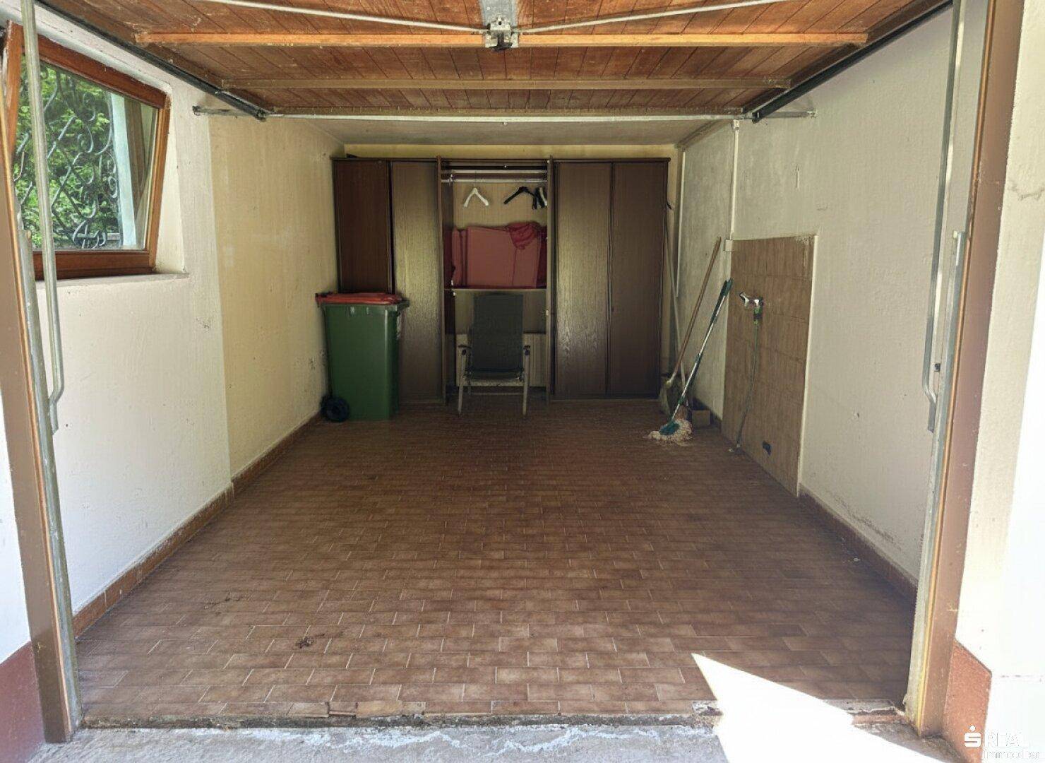 Geräumige Garage mit Fliesenboden und Stauraum, ideal für Fahrzeuge und Lagerung.