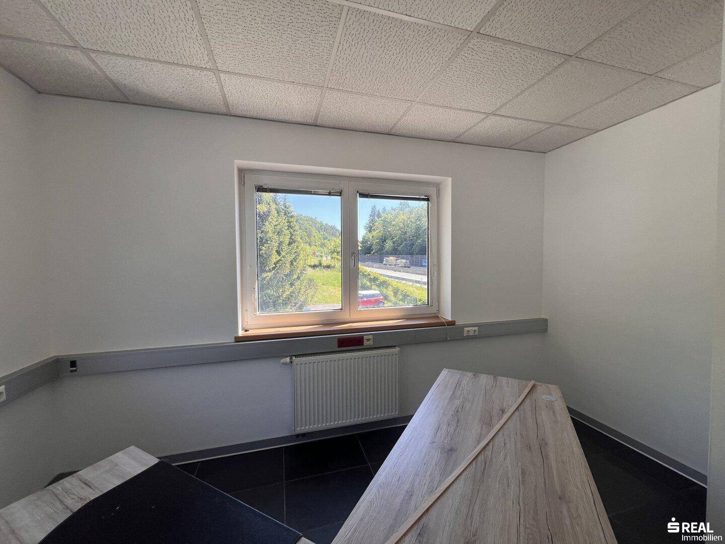 Büro mit einem Fenster, dunklem Fliesenboden und einem Teil eines Eckschreibtisches.