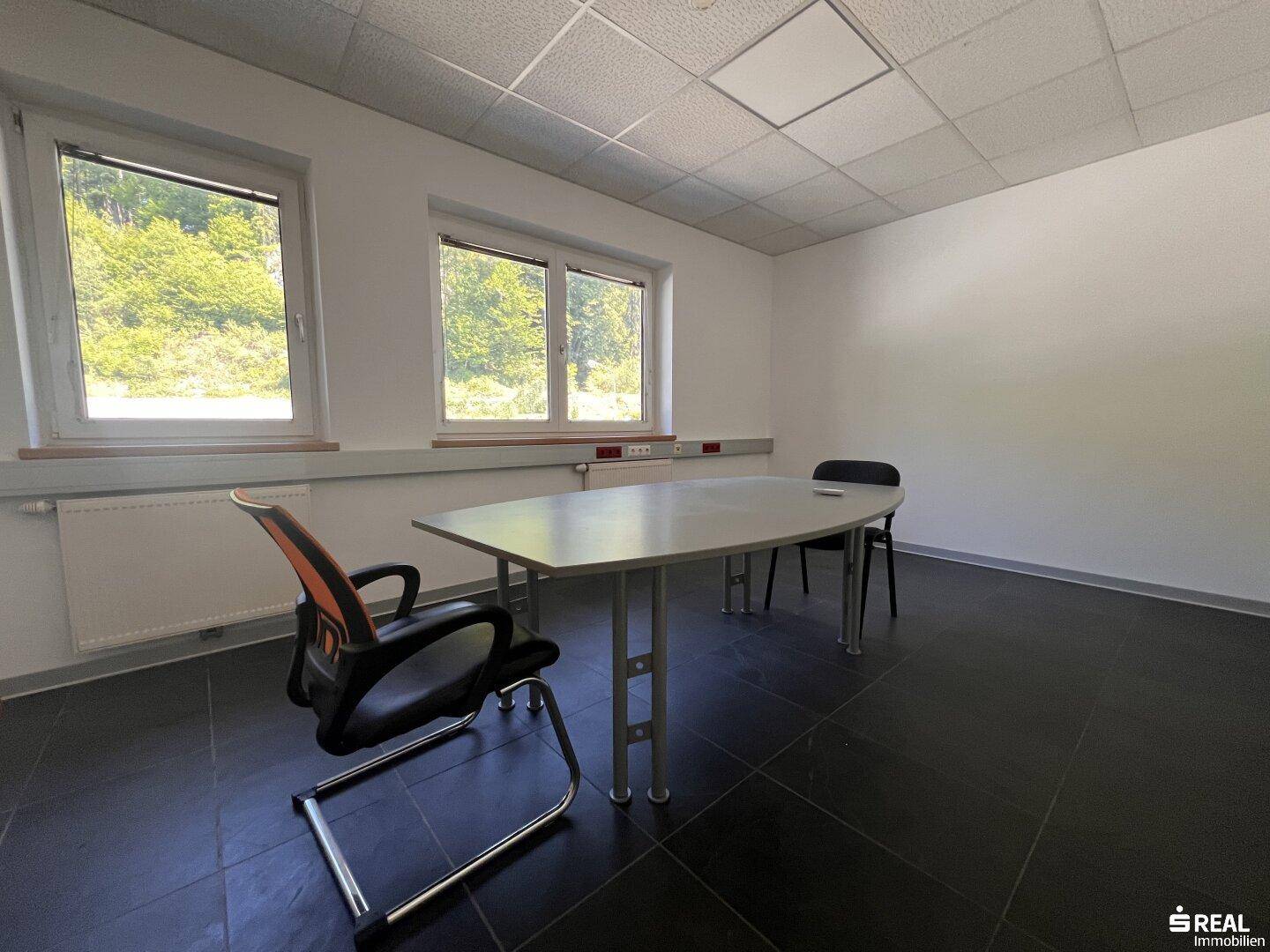 Büro mit dunklem Fliesenboden, einem Tisch und Stühlen sowie Fenstern mit Ausblick.