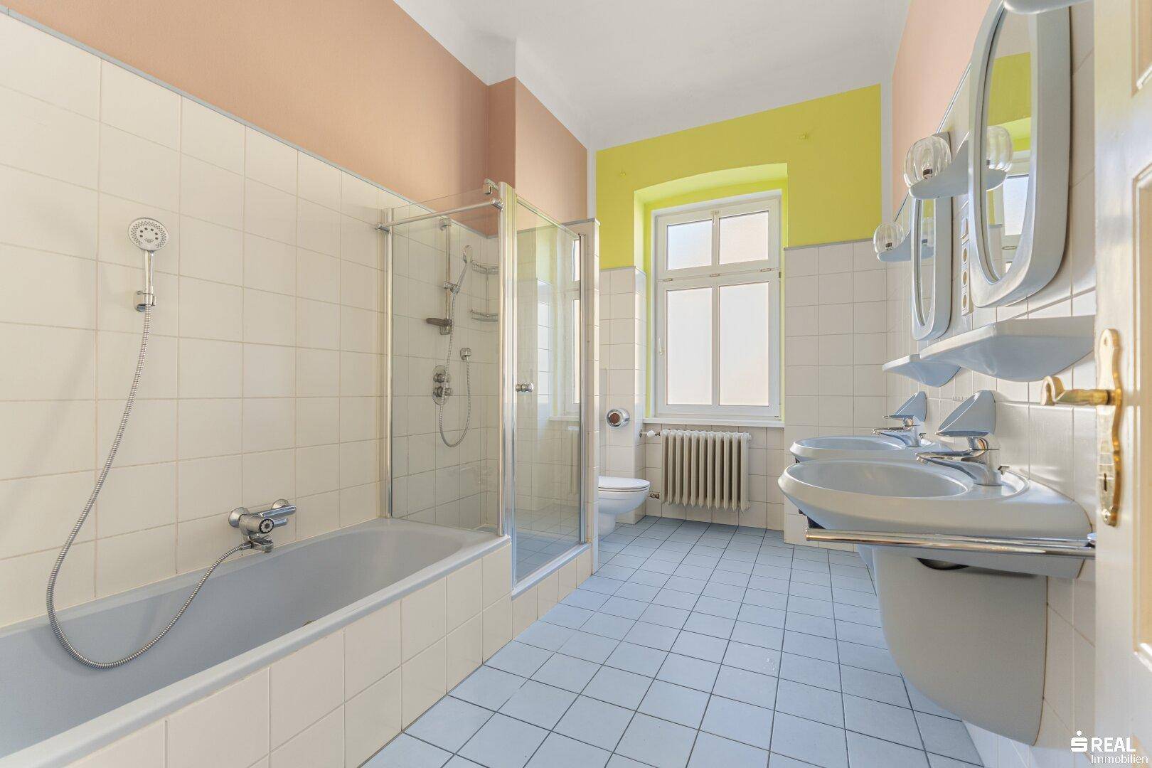 Geräumiges Badezimmer mit Badewanne, Duschkabine, zwei Waschbecken und Fenster.