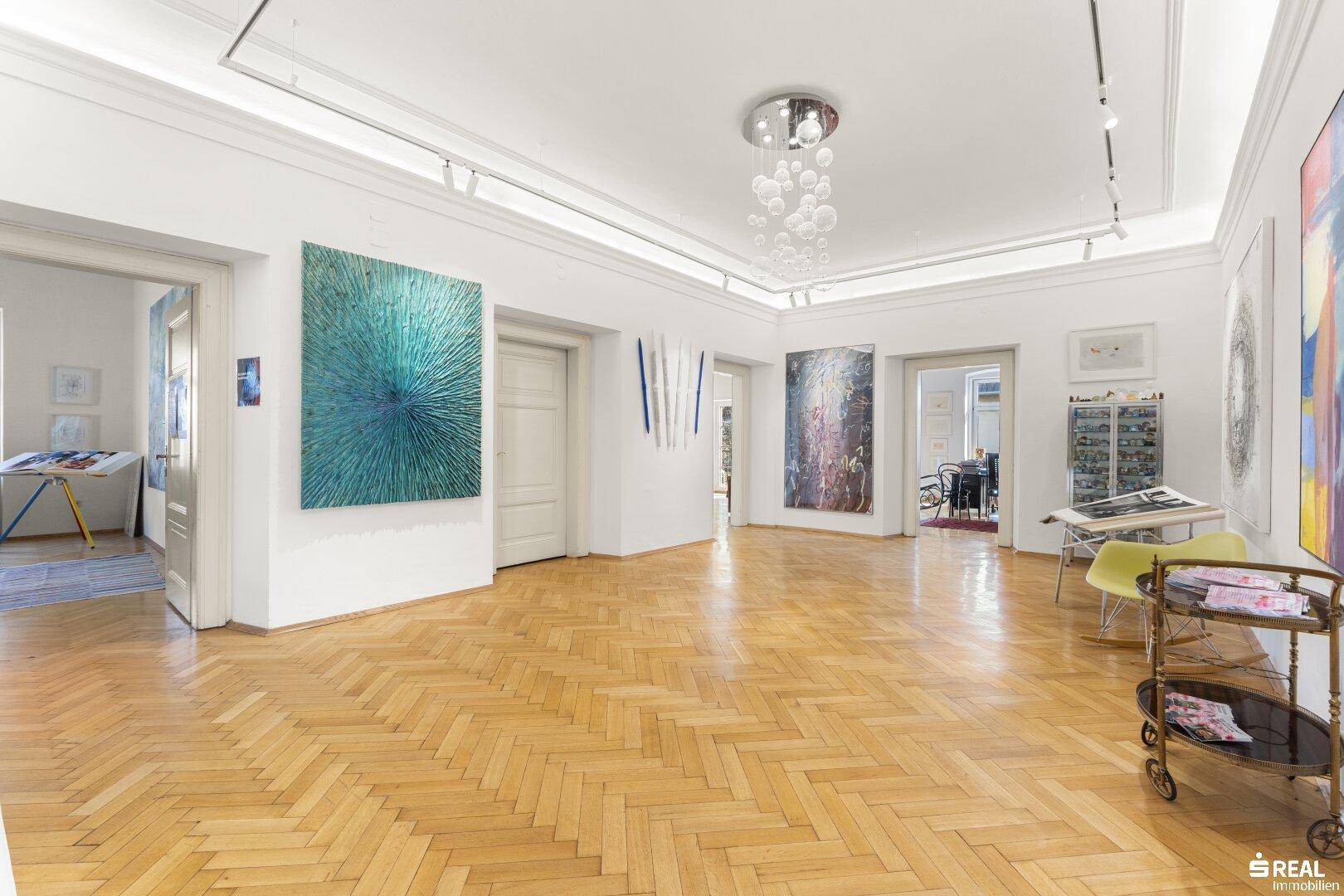 Heller, weitläufiger Raum mit Fischgrätparkett, moderner Beleuchtung und vielfältigen Kunstwerken.