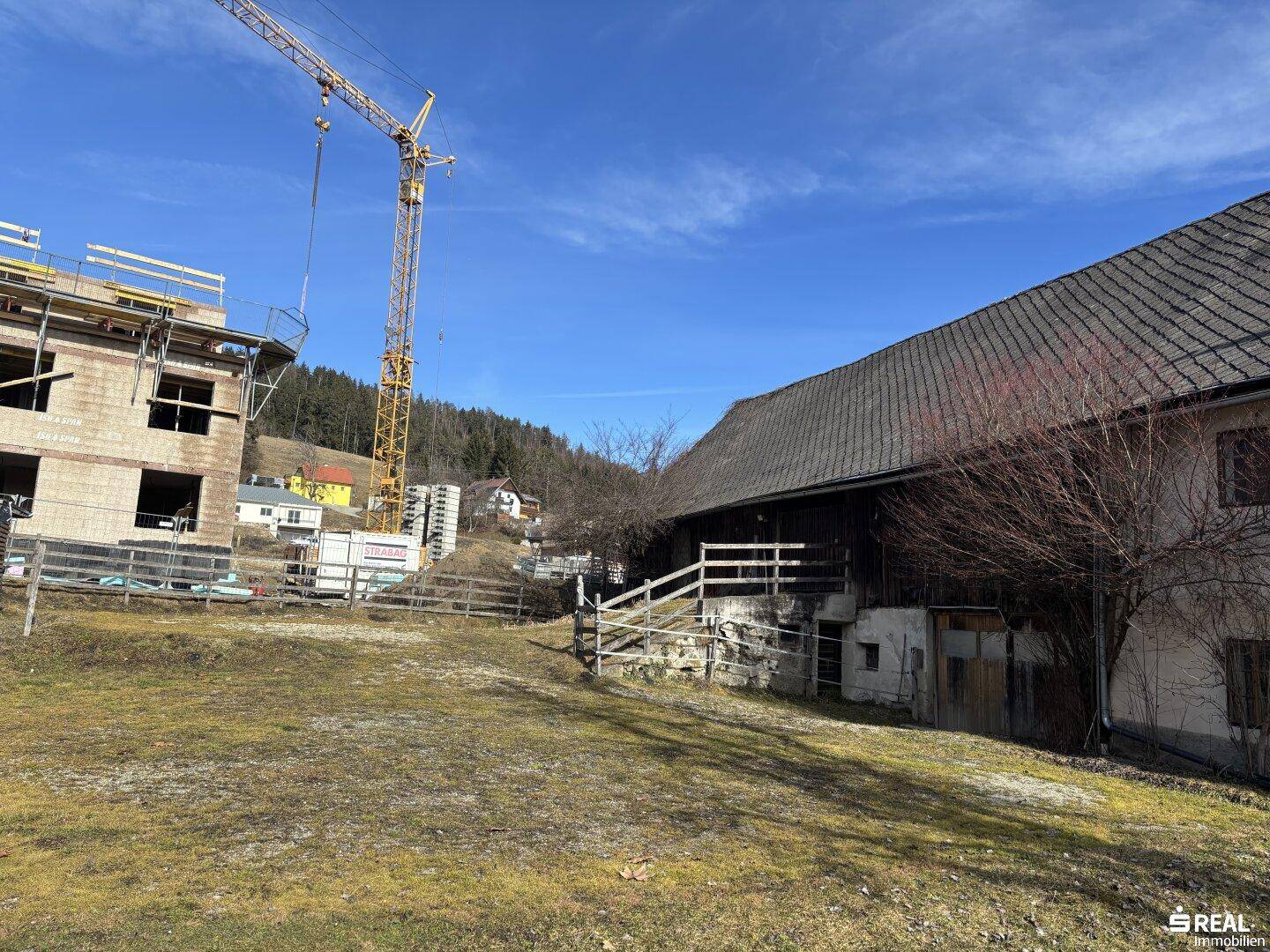 Blick auf das historische Gebäude und eine angrenzende Baustelle mit Kran unter blauem Himmel.