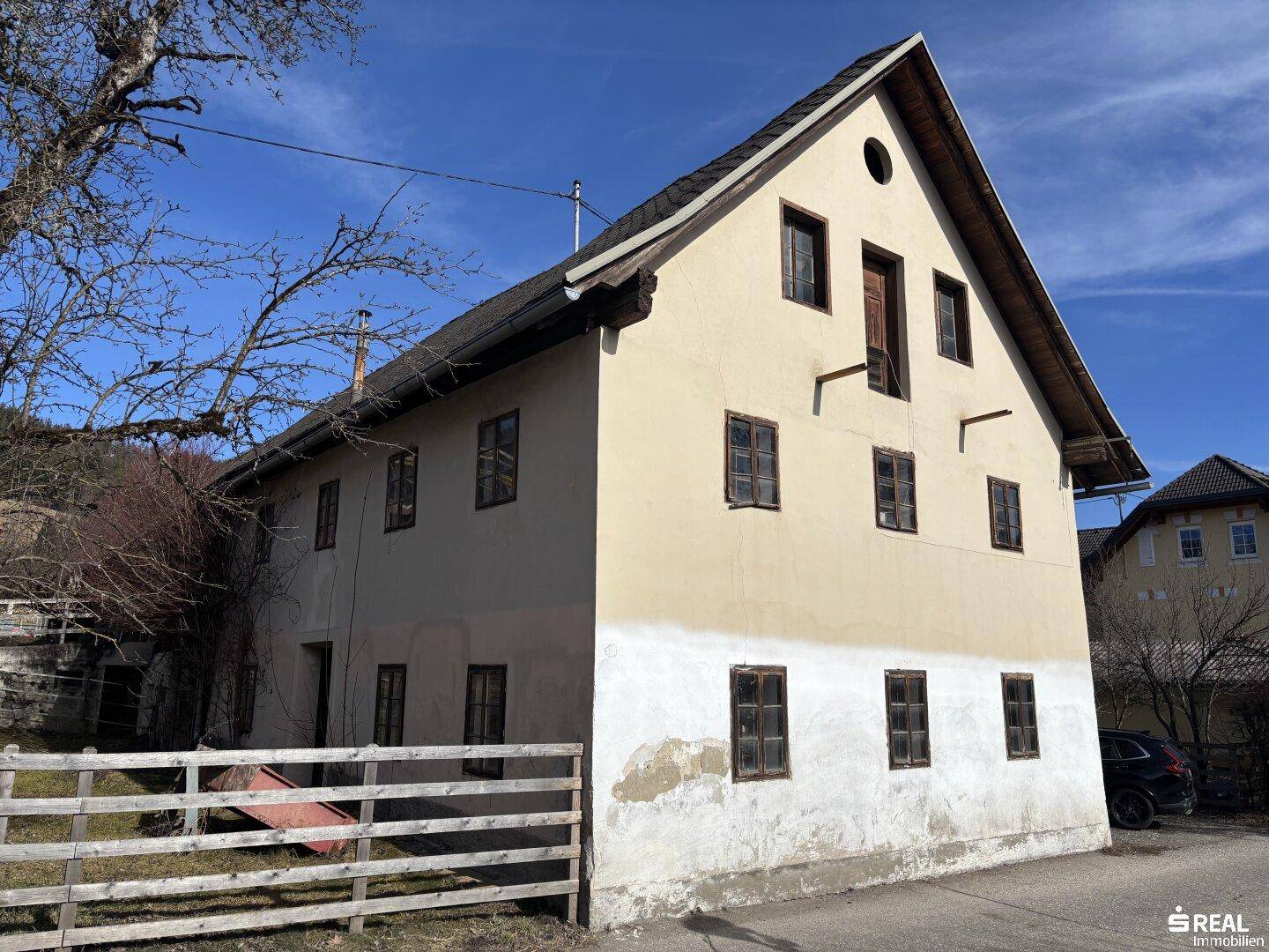 Seitenansicht des alten Gebäudes mit Putzfassade und traditionellen Holzfenstern unter blauem Himmel.