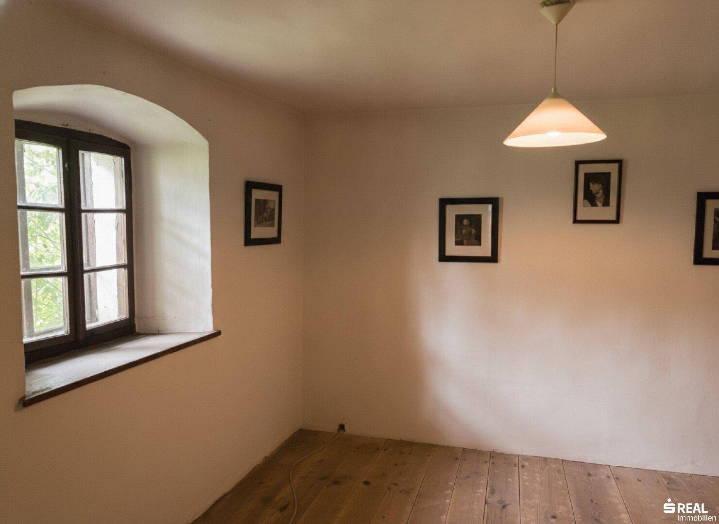 Helle Zimmerecke mit einem Fenster, Holzdielenboden und schlichter Wanddekoration.