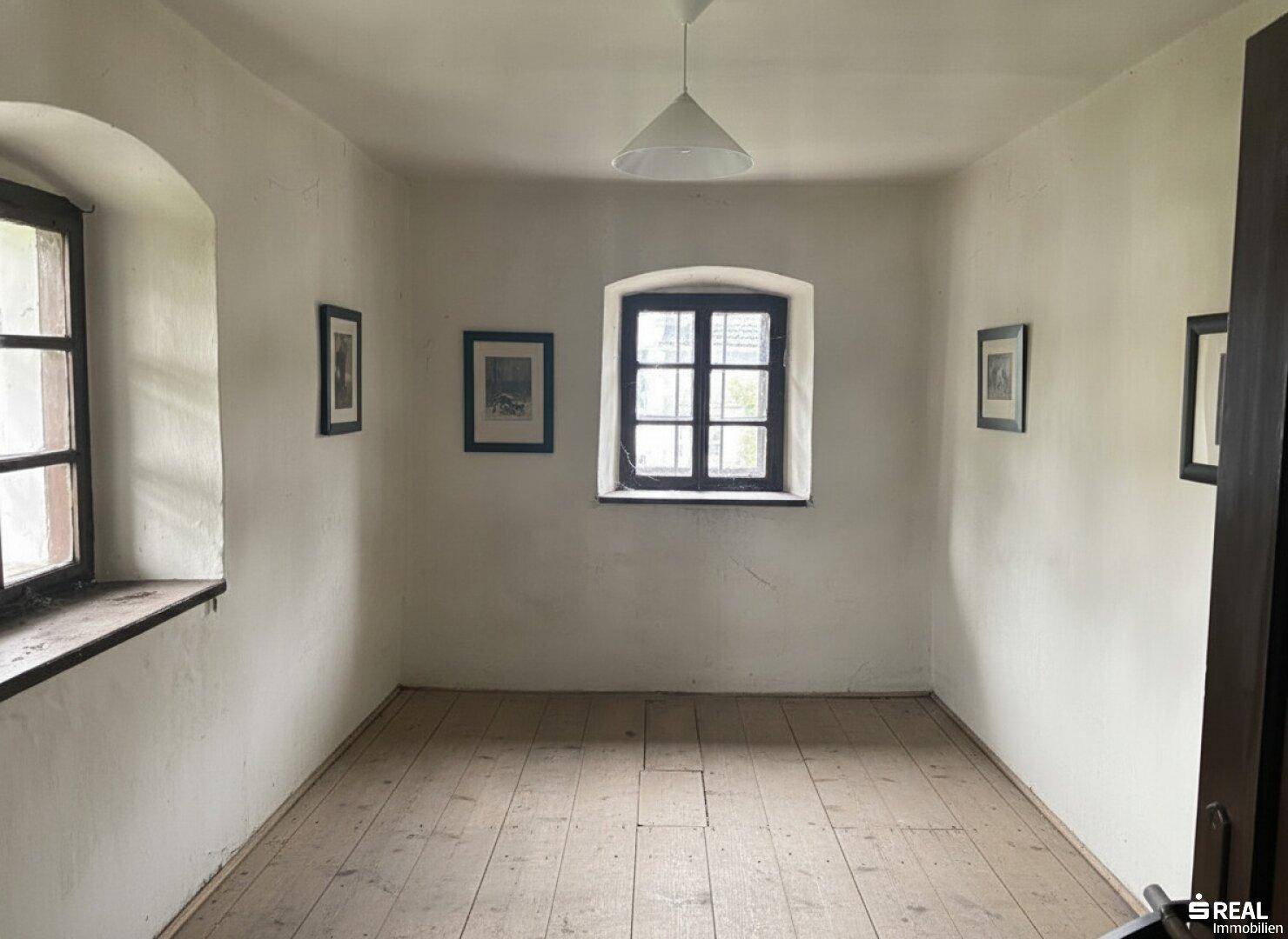 Einfacher Raum mit Holzdielenboden, drei Fenstern und einer Deckenleuchte, bereit zur Gestaltung.