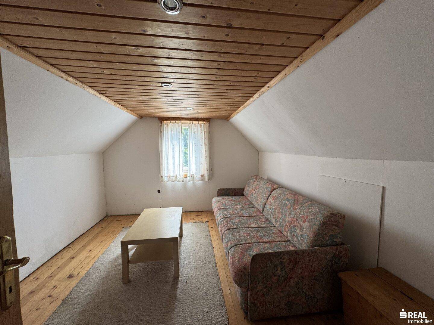 Gemütliches Zimmer im Dachgeschoss mit Holzdecke, Teppich und Sofa.