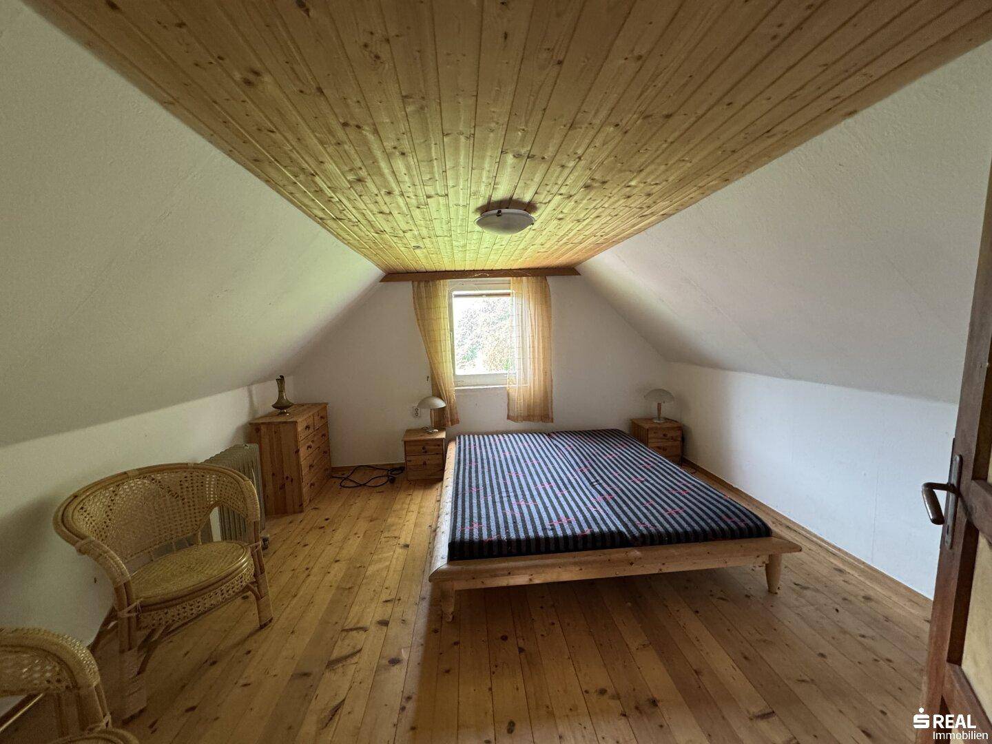 Schlafzimmer im Dachgeschoss mit Holzdecke, Holzboden und Doppelbett.