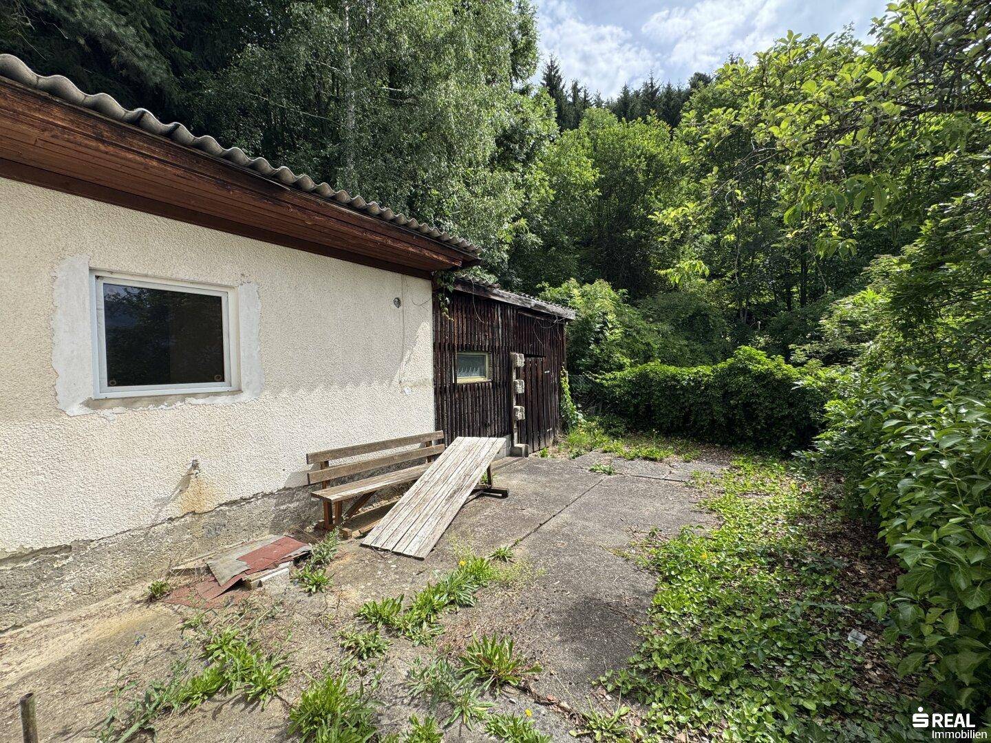 Einfache Terrasse am Haus mit Holzbänken und Blick ins Grüne.