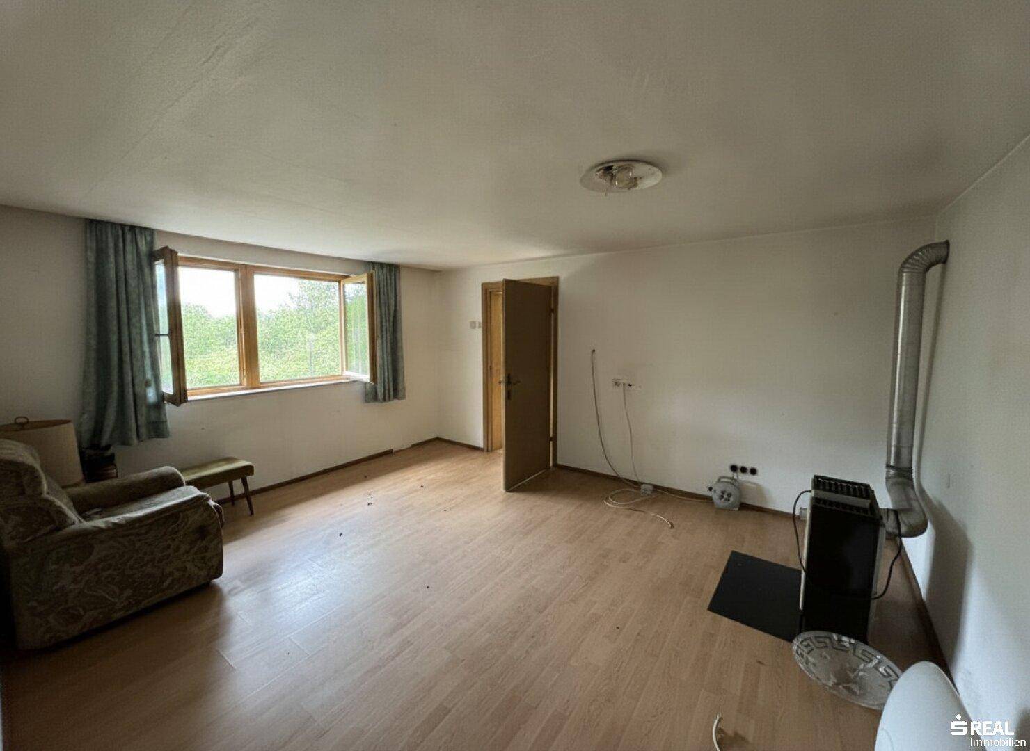Geräumiges Wohnzimmer mit Laminatboden, Holzofen und Blick ins Grüne.
