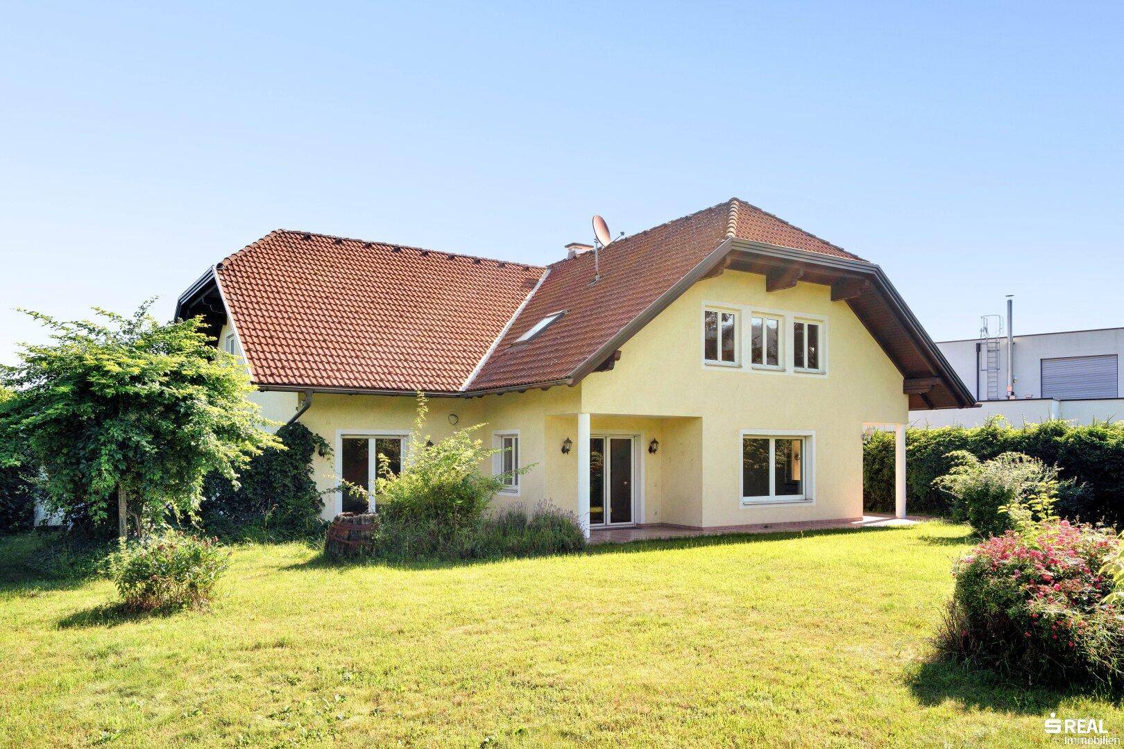 Rückansicht des Hauses mit großem Garten, Rasenfläche und Zugang zur Terrasse an einem sonnigen Tag.