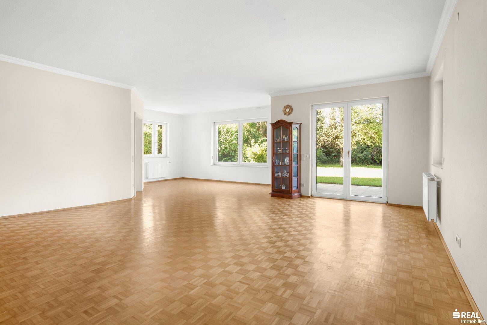 Helles Wohnzimmer mit Fischgrätparkett, großen Fenstern und direktem Zugang zum Gartenbereich.