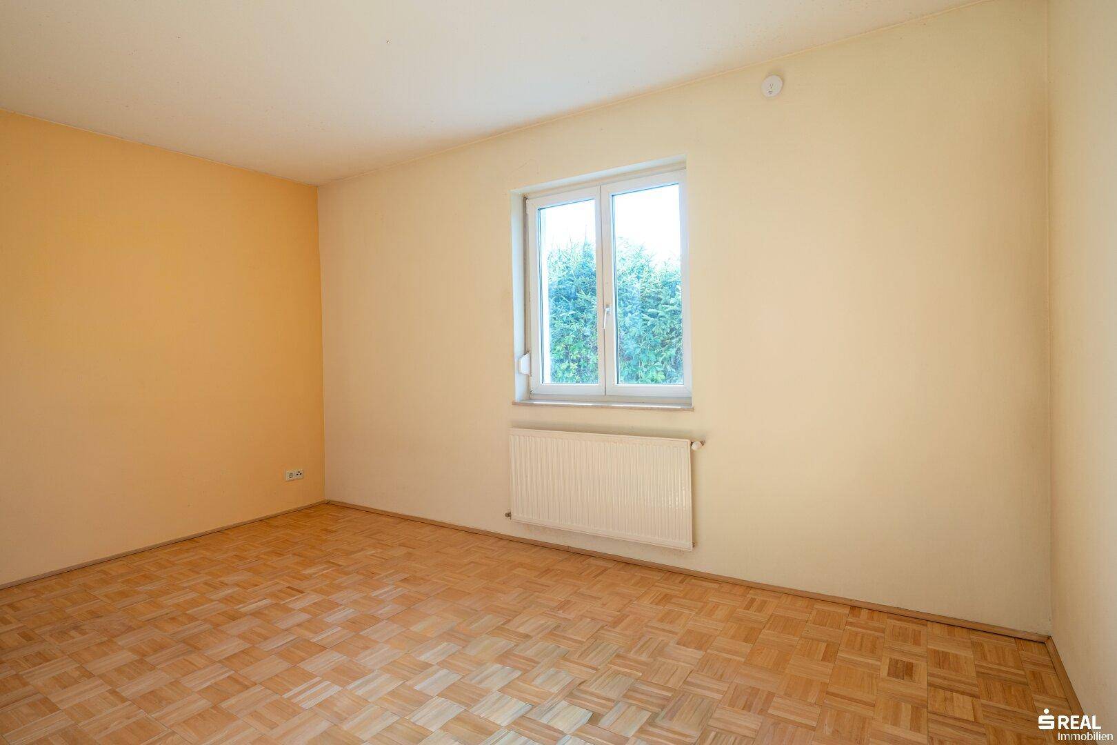Schlafzimmer mit Parkettboden, hellem Fenster und Blick ins Grüne, ideal für Ruhe und Entspannung.