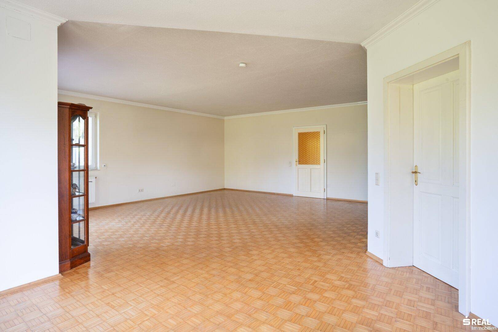 Geräumiges Wohnzimmer mit Parkettboden und klassischer Holztür, bereit zur individuellen Gestaltung.