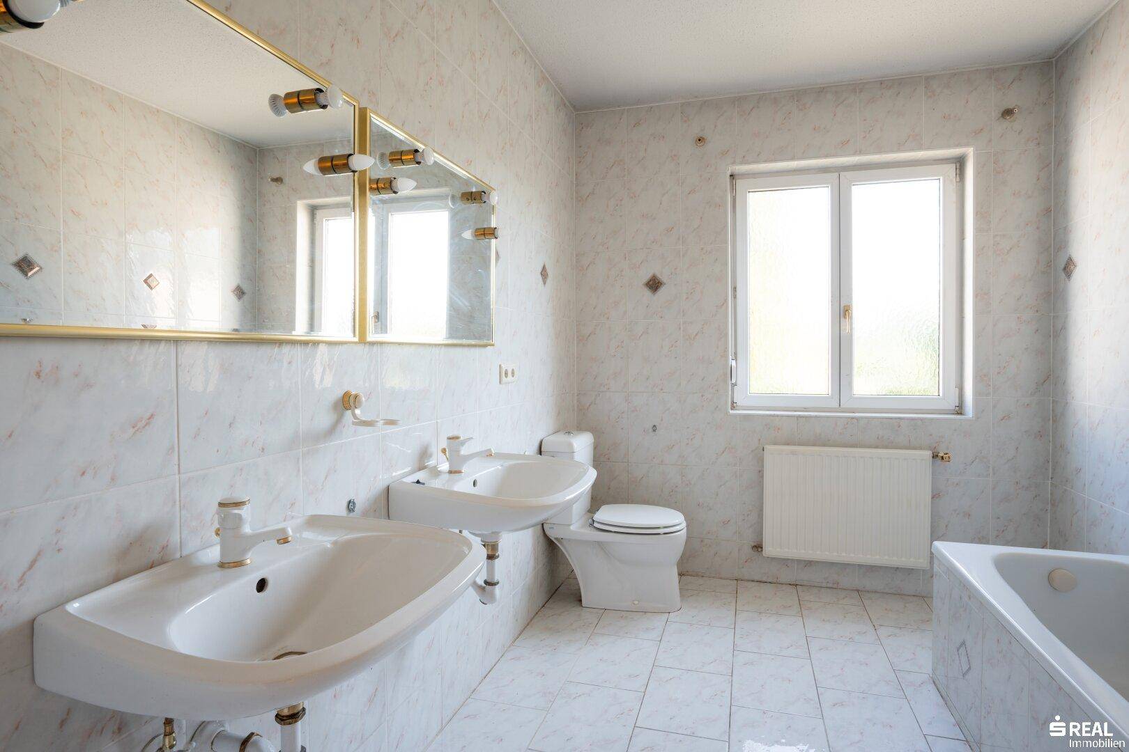 Gefliestes Badezimmer mit Doppelwaschbecken, Badewanne, WC und Bidet, ausgestattet mit Fenster.