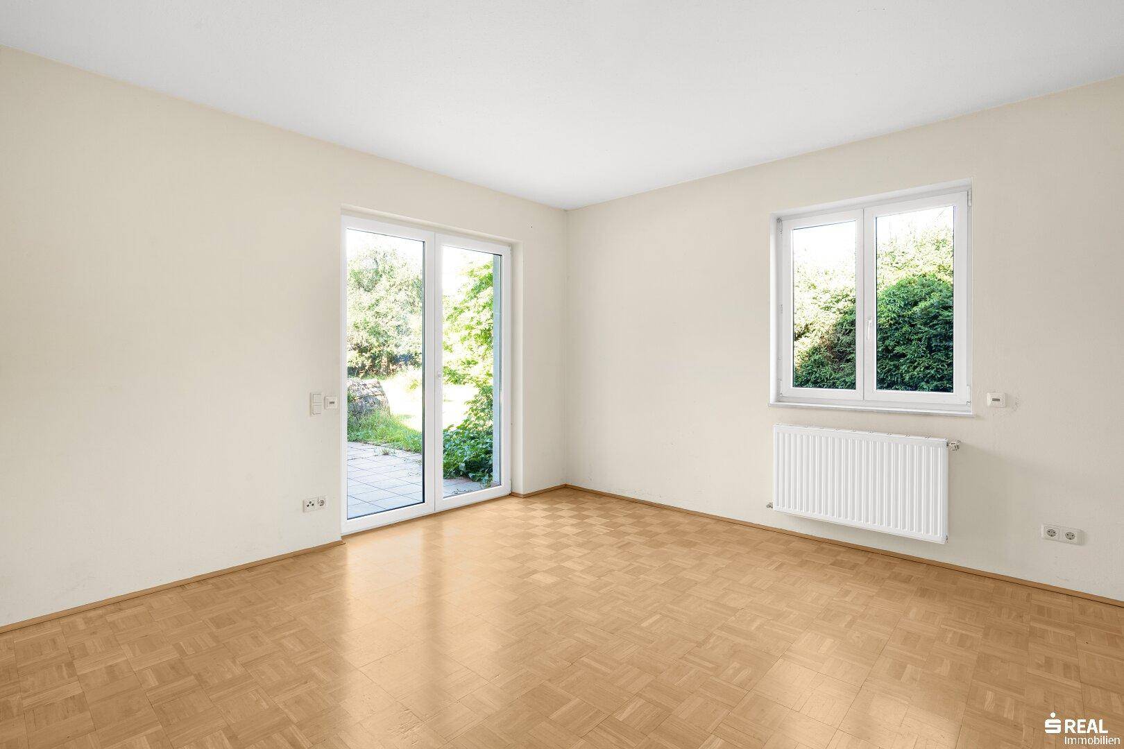 Helles Zimmer mit Parkettboden und großem Schiebetürzugang zum Außenbereich, bietet viel Tageslicht.