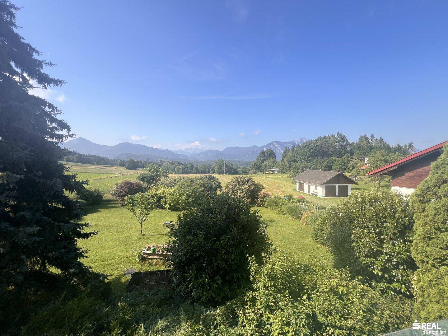 Sonniger, weitläufiger Garten mit gepflegtem Rasen und üppiger Vegetation, bietet einen malerischen Blick auf die Berge.