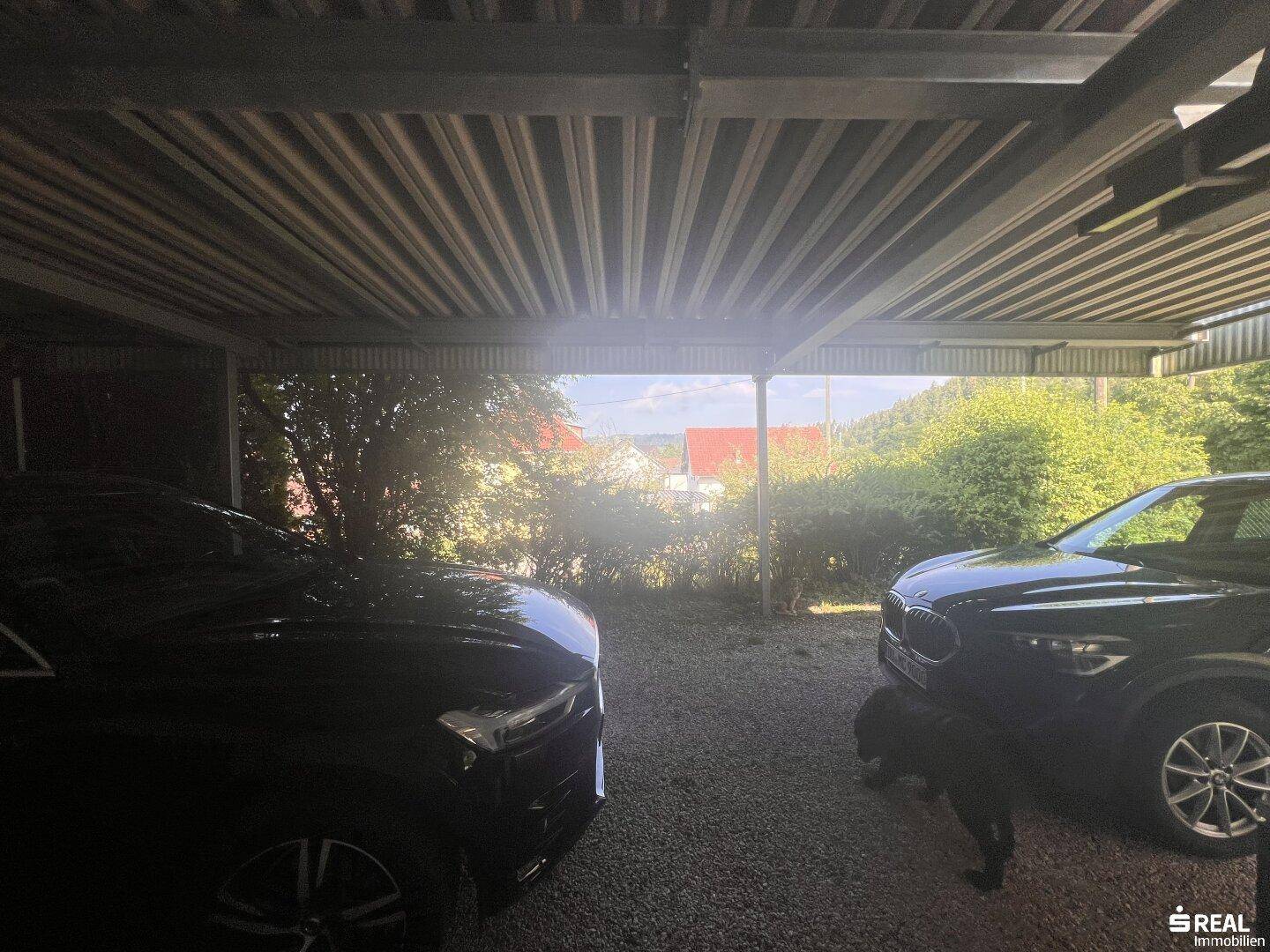 Überdachter Carport mit Platz für zwei Fahrzeuge auf Kiesboden, bietet Schutz vor Witterungseinflüssen.