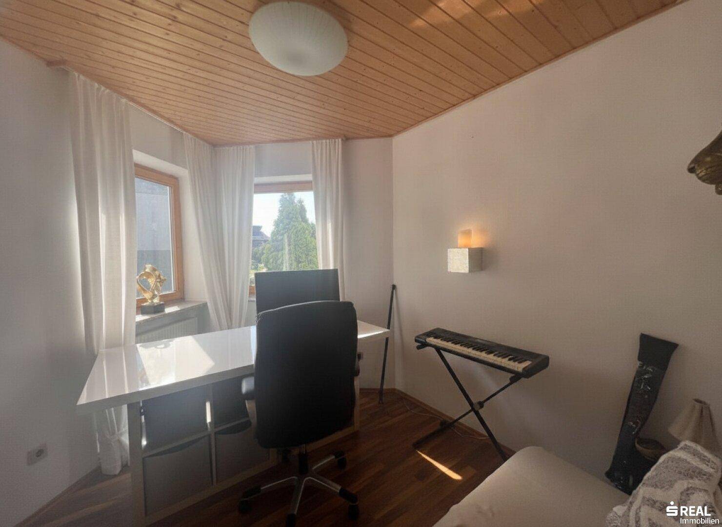 Helles Arbeitszimmer mit weißem Schreibtisch, Bürostuhl und Holzdecke, ideal für konzentriertes Arbeiten.