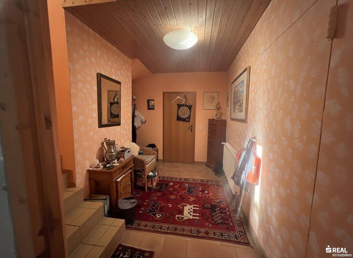 Einladender Flur mit gemusterter Tapete, Holzdecke und Fliesenboden, führt zu einer Treppe.