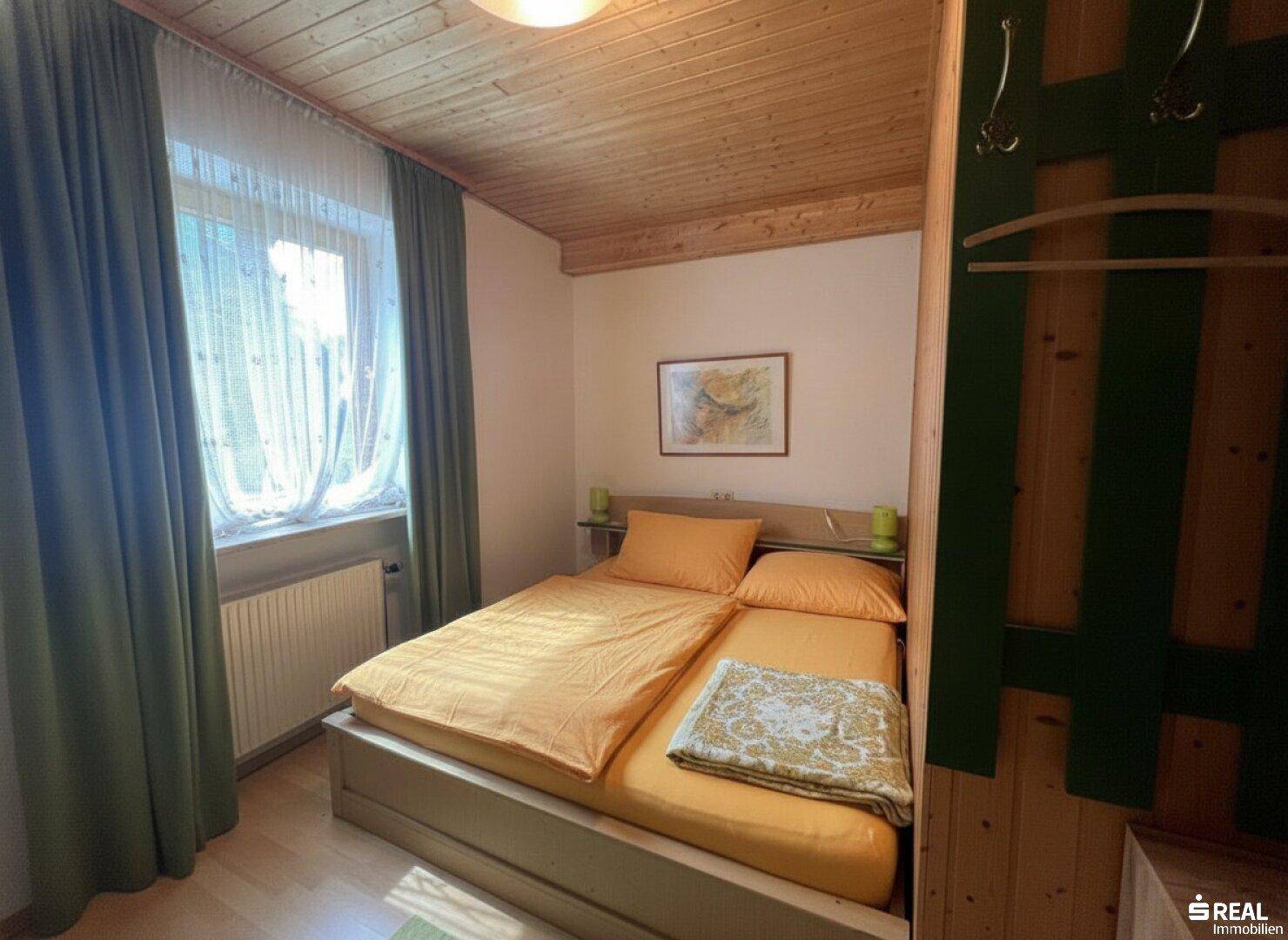 Gemütliches Schlafzimmer mit zwei Einzelbetten, grünen Vorhängen und Holzwänden, unter einer Holzdecke.