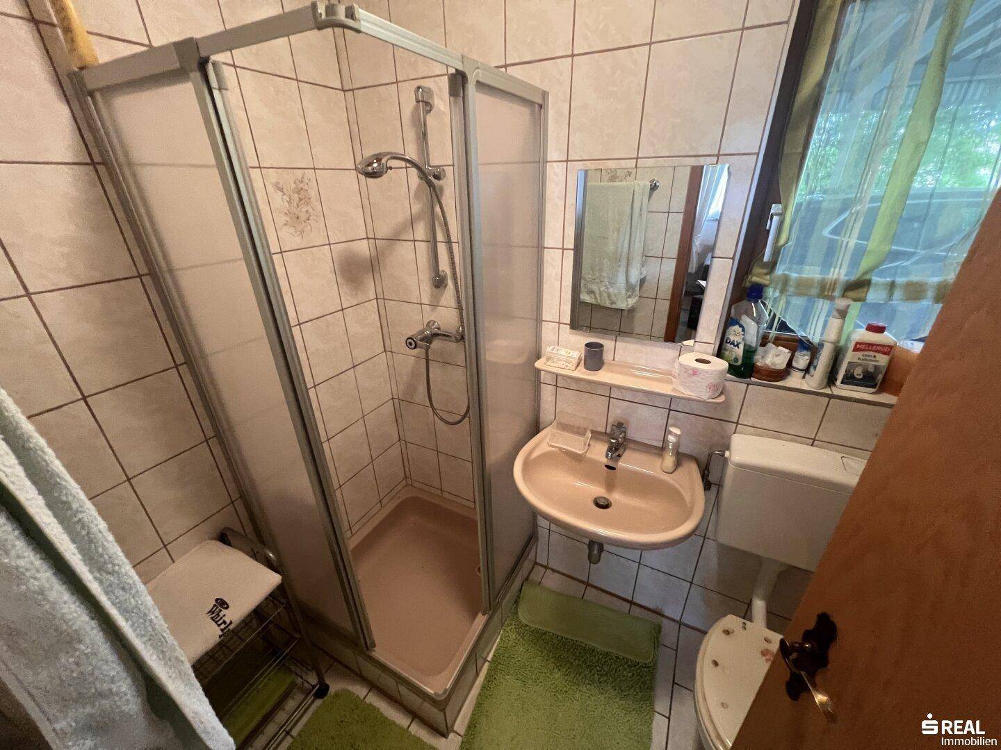 Kleines Badezimmer mit weißen Fliesen, Duschkabine, Waschbecken und WC, ausgestattet mit einer Holzdecke.