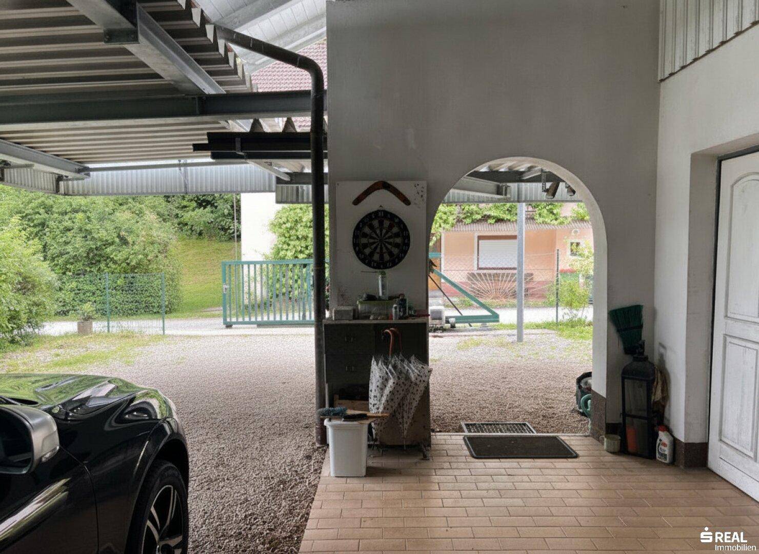 Überdachter Stellplatz mit Dartscheibe und Blick ins Grüne, ideal für Freizeitaktivitäten.