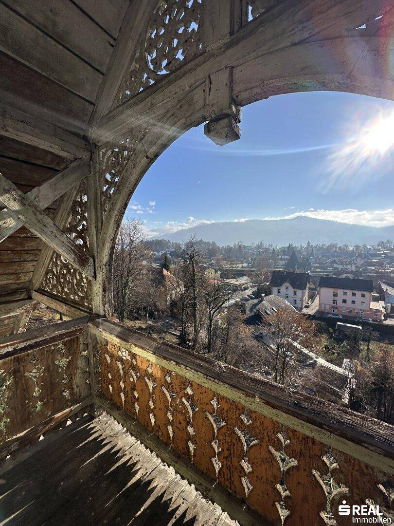 Alter, kunstvoll geschnitzter Holzbalkon mit weitem Blick über die Stadt und die umliegenden Berge an einem sonnigen Tag.
