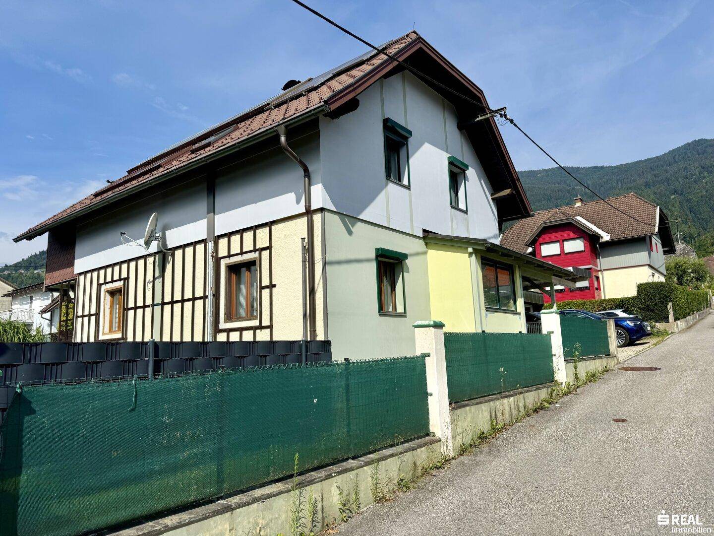 Seitenansicht des Hauses mit traditioneller Fassade und grüner Hecke entlang der Straße.