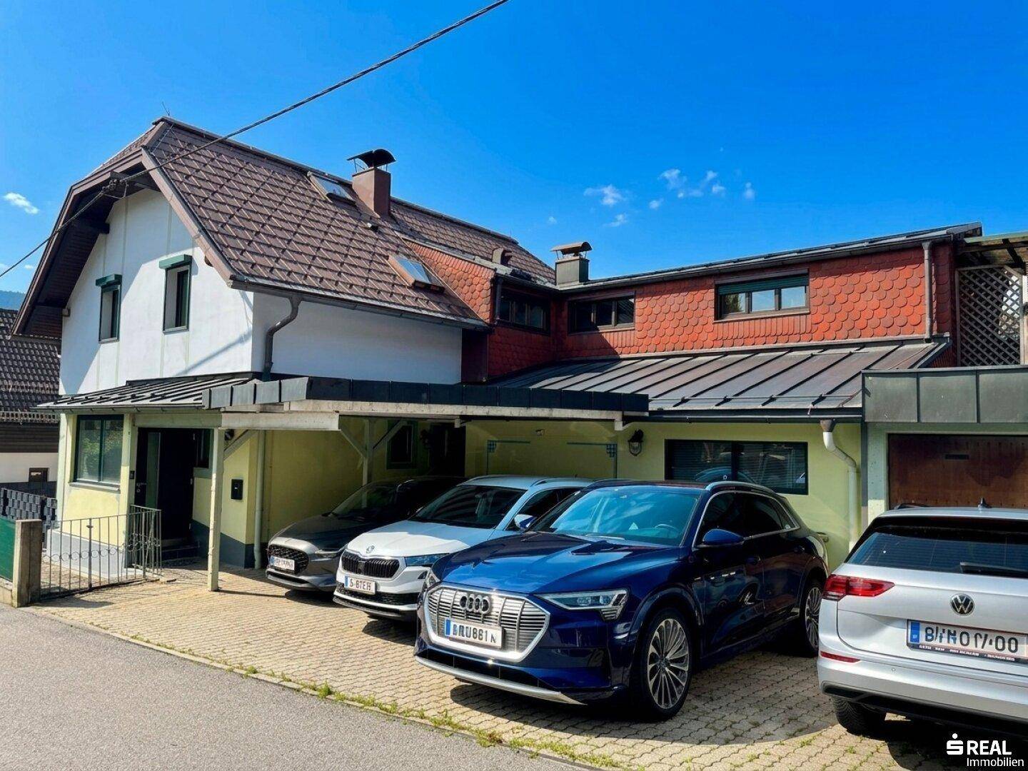 Vorderansicht des Hauses mit Carport und mehreren geparkten Autos unter klarem Himmel.