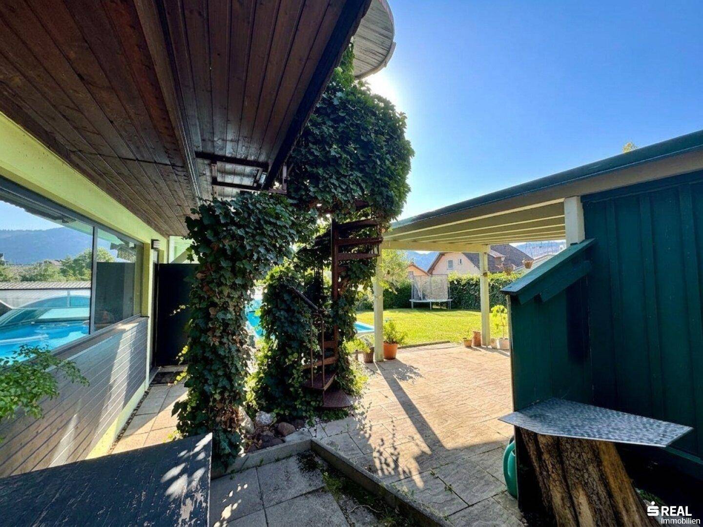 Überdachter Außenbereich mit bewachsener Wendeltreppe und Blick auf den Pool und die Berge.