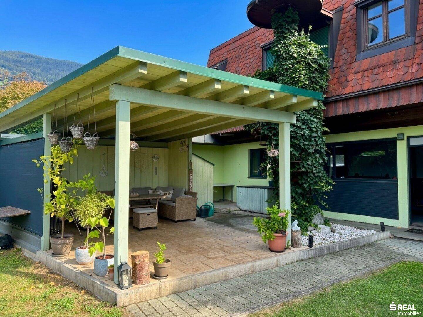 Gemütlicher überdachter Terrassenbereich mit Loungemöbeln und Topfpflanzen im Garten.