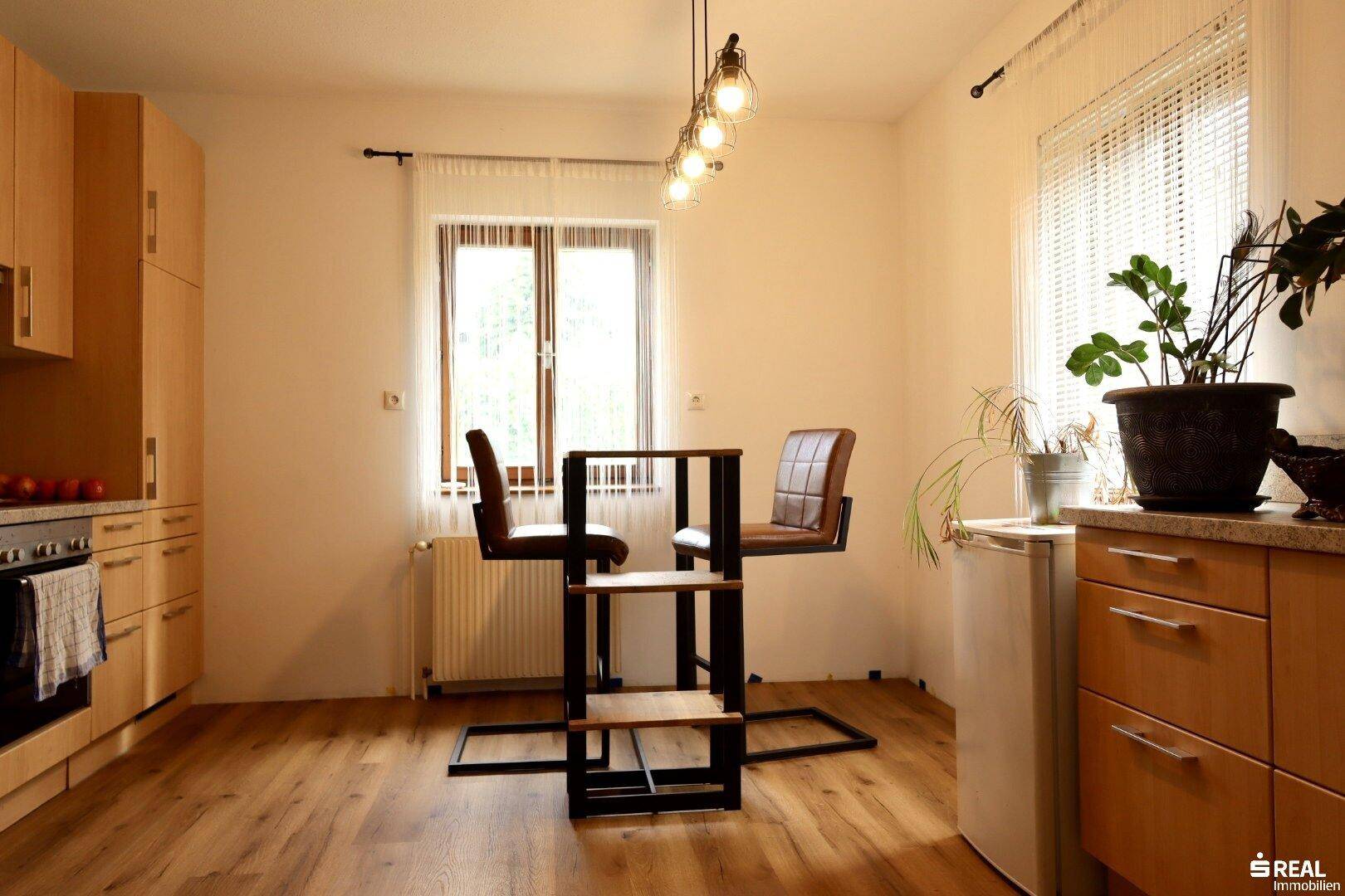 Helle Küche mit Holzboden, Einbauschränken und kleinem Frühstücksbereich am Fenster.