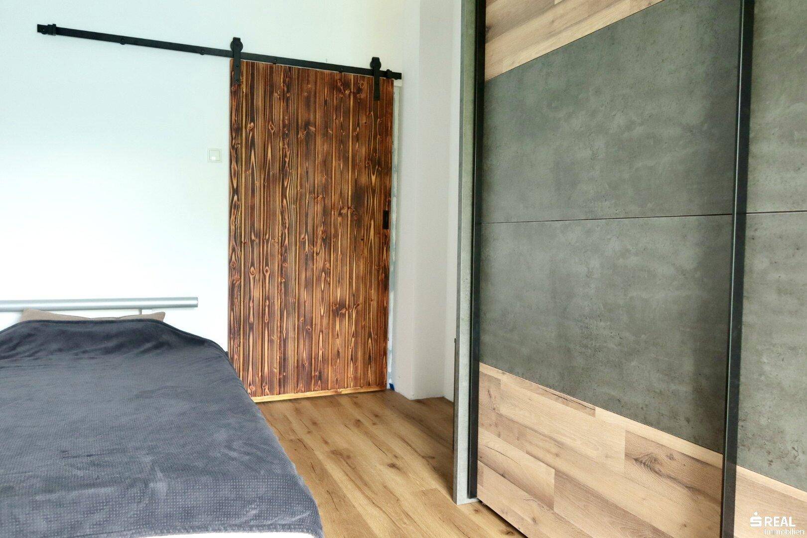 Schlafzimmer mit Holzboden, moderner Schiebetür und integriertem Kleiderschrank.