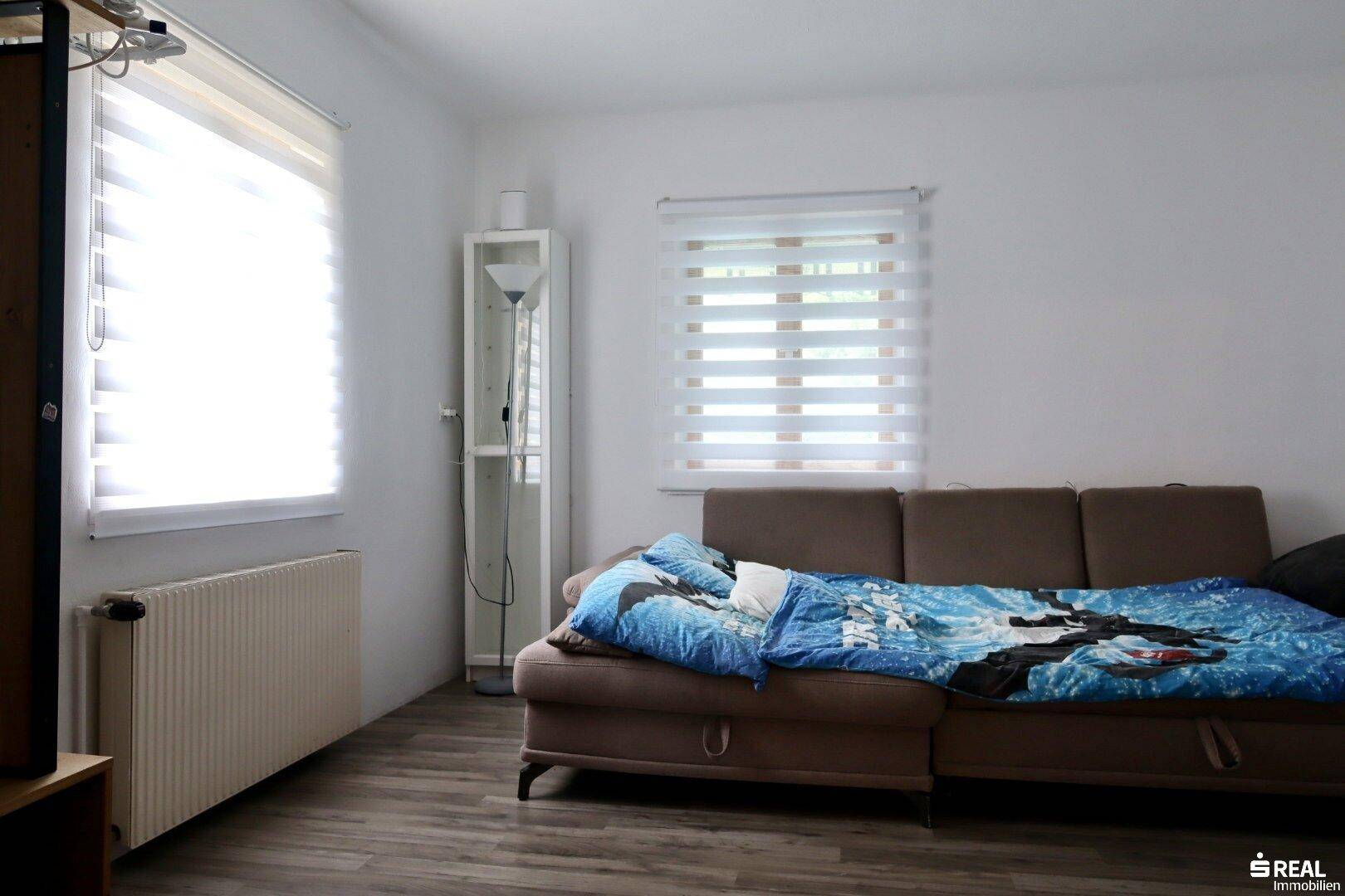 Gemütliches Wohnzimmer mit Sofa, Holzboden und großen Fenstern für viel Tageslicht.