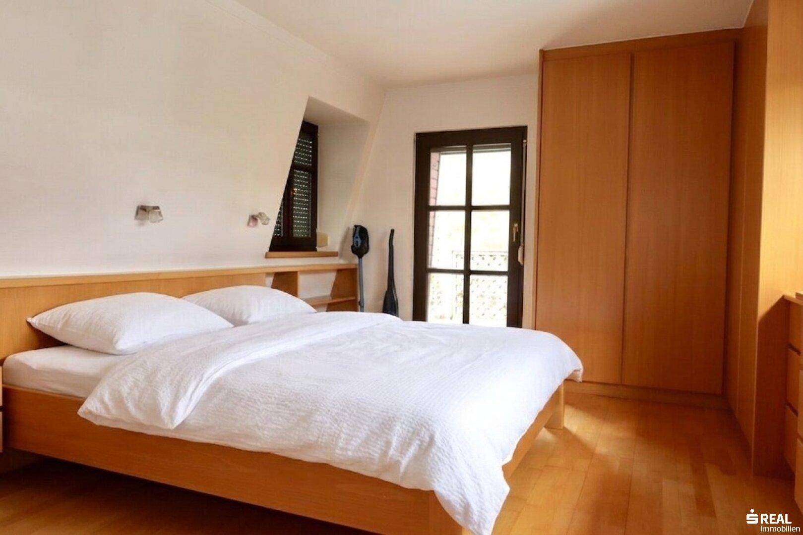 Schlafzimmer mit Holzboden, Einbauschränken und Zugang zu einem Balkon.