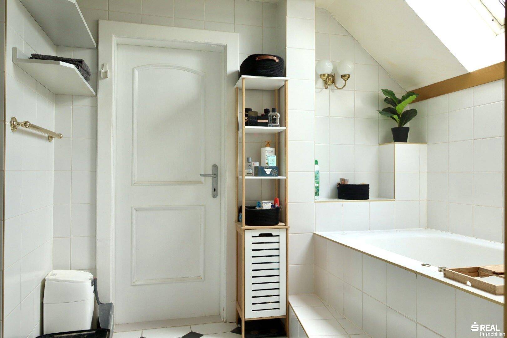 Badezimmer mit Badewanne, weißen Fliesen und Dachschräge, bietet Stauraum.