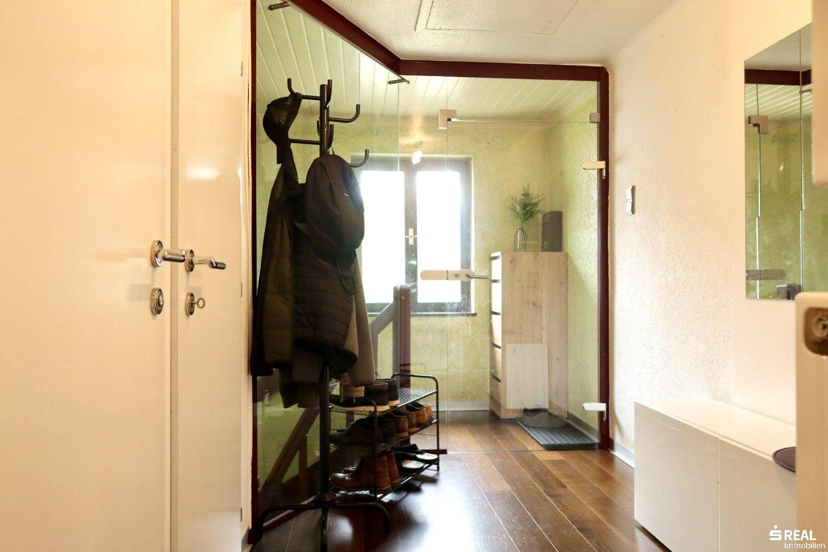 Heller Flur mit Holzboden, Garderobe und einer modernen Glasabtrennung.